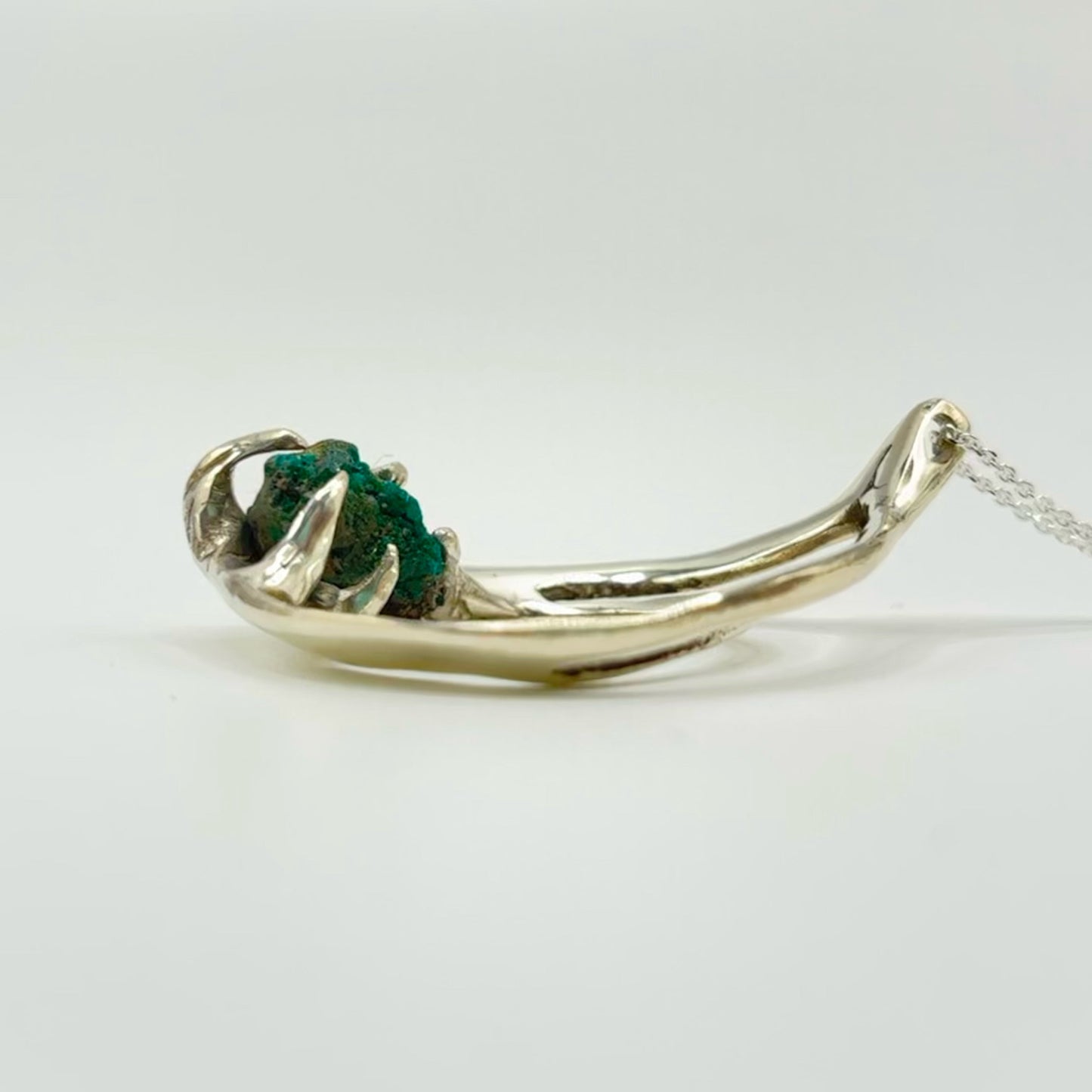Silver necklace with a unique pendant on a light gray background, raw dioptase in the center.