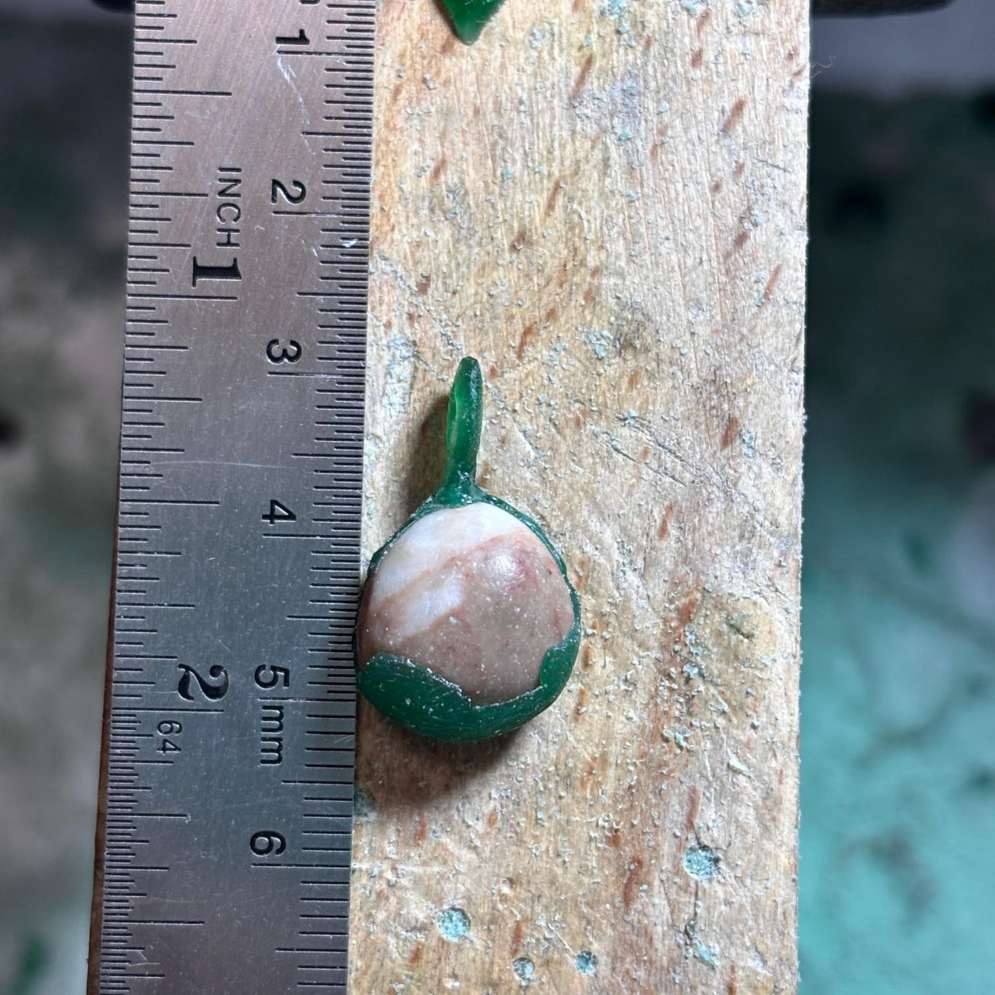Small stone in wax on a wooden surface next to a ruler for scale.