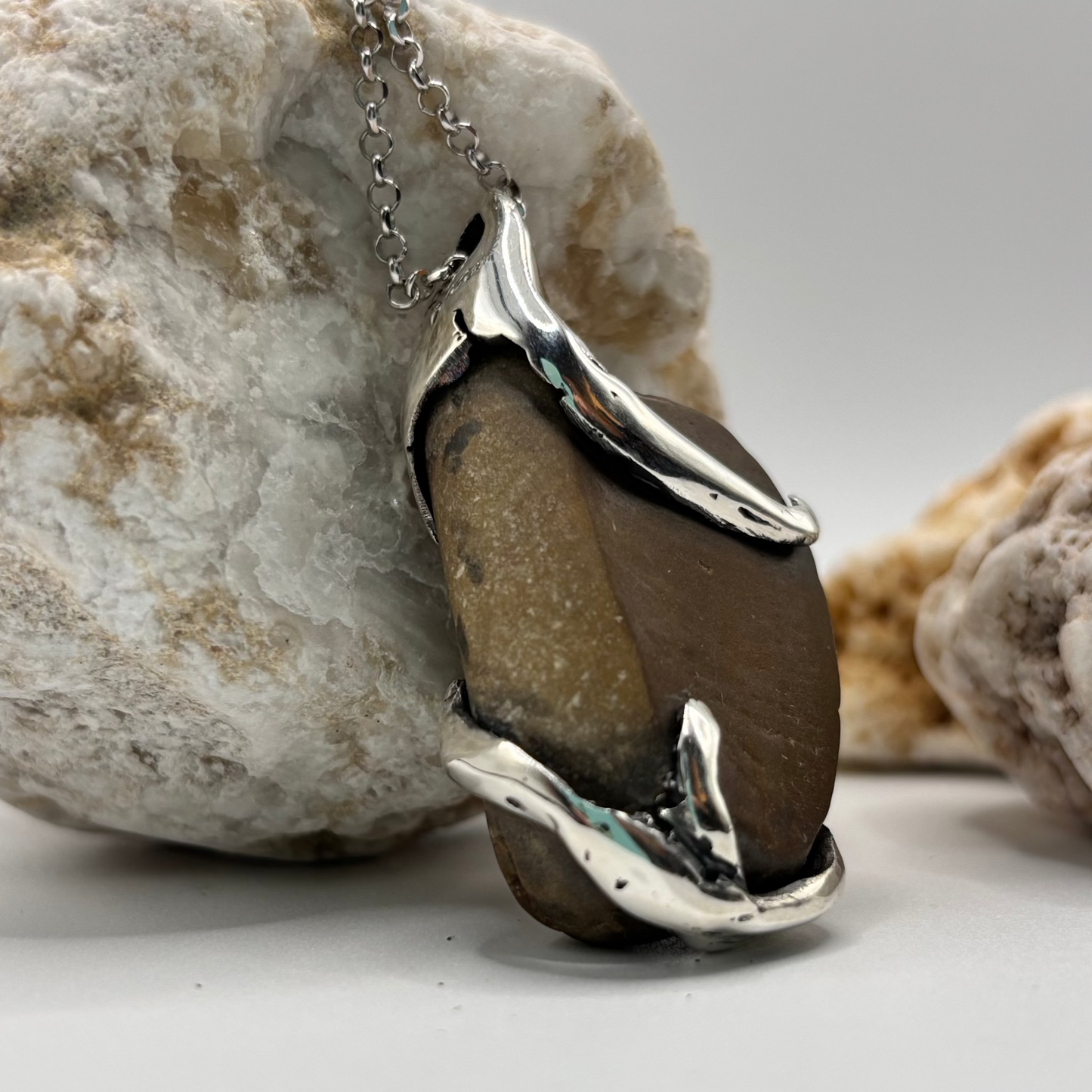 Close-up of a handmade pendant with a raw beach stone encased in an organic silver design.