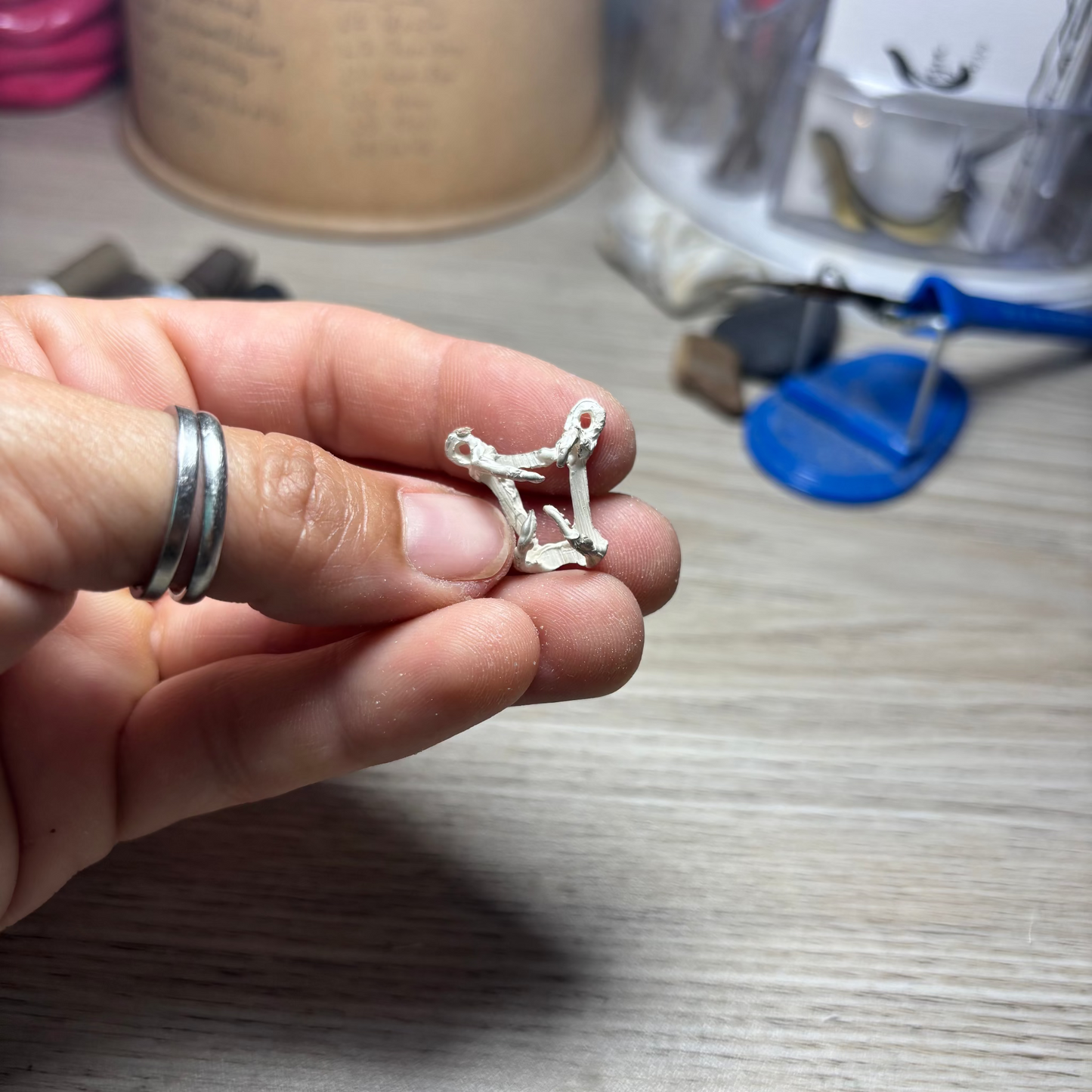 Hand holding a small silver skeleton pendant charm with a blurred background