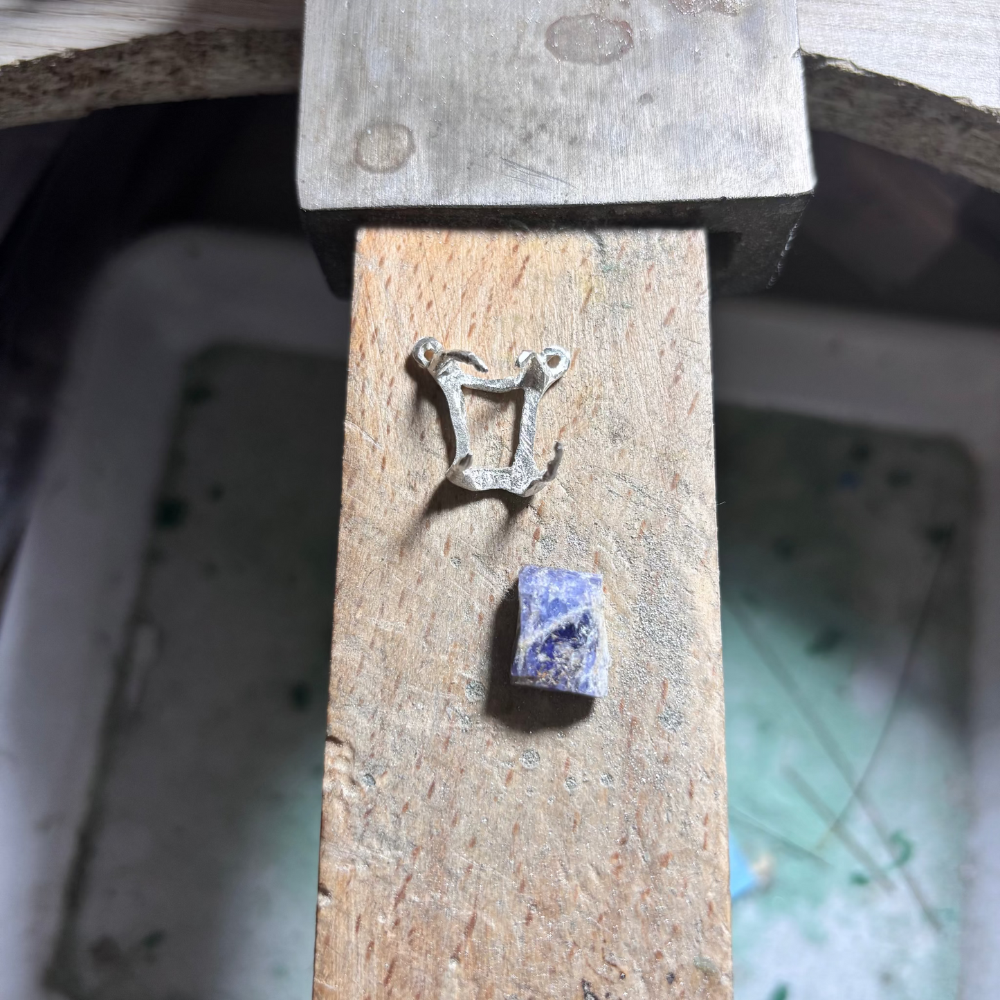 Silver harp-shaped pendant and blue tanzanite raw stone on a wooden block
