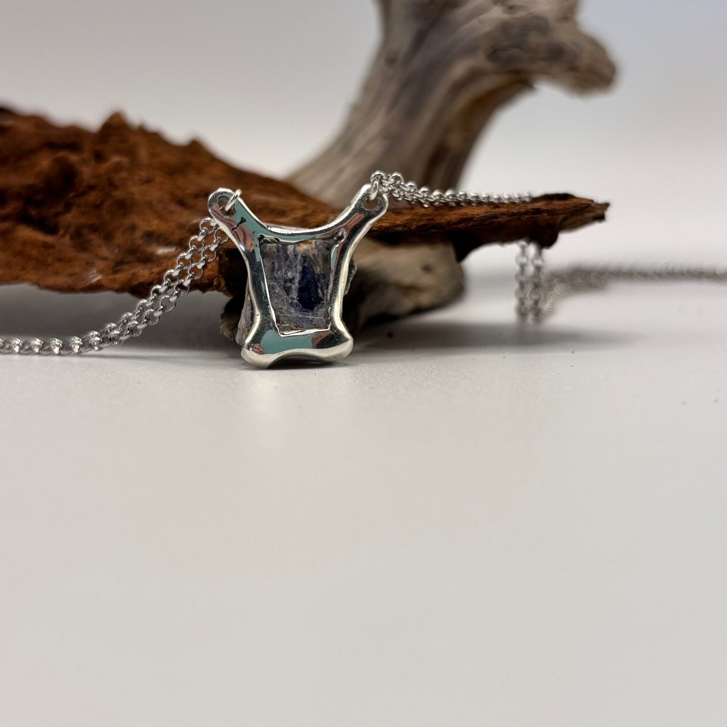 the back of a Silver necklace with a unique pendant on a neutral background