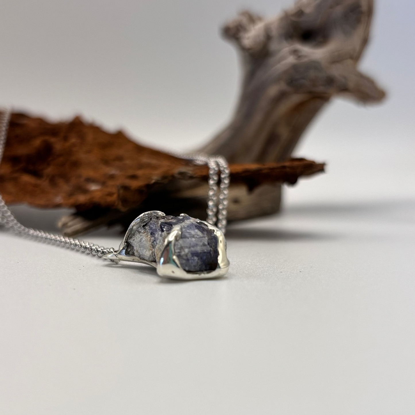 Silver necklace with a tanzanite raw pendant on a neutral background