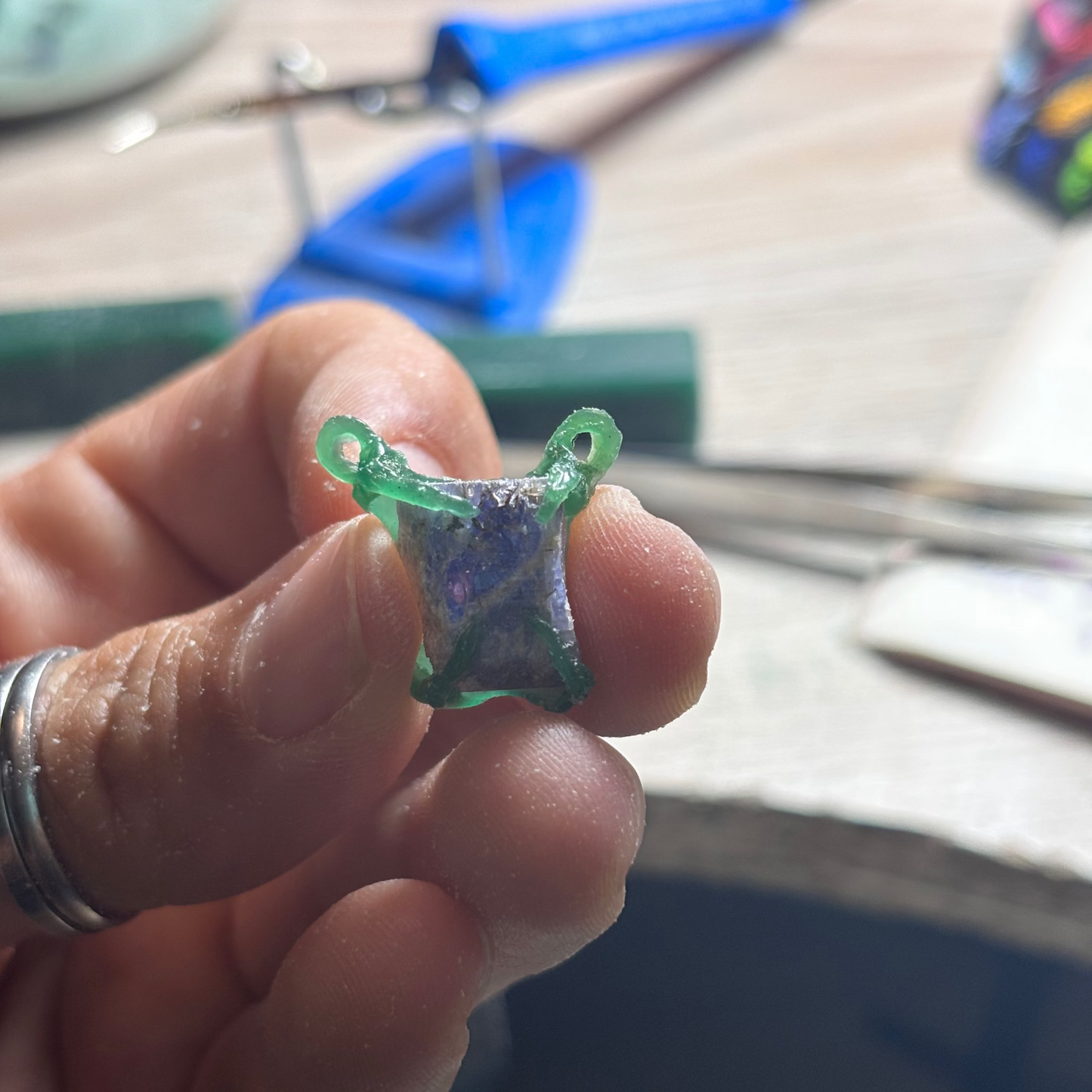 Hand holding the pendant in green wax holding with four claws a raw tanzanite. jewelry made using the lost wax method. soon to be set in silver.