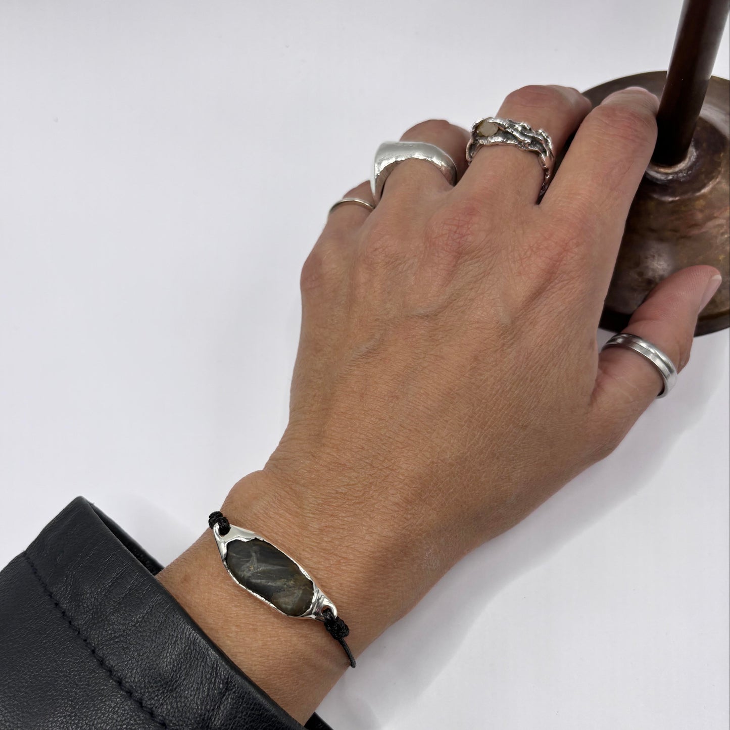Hand wearing multiple silver rings and a bracelet on a white background