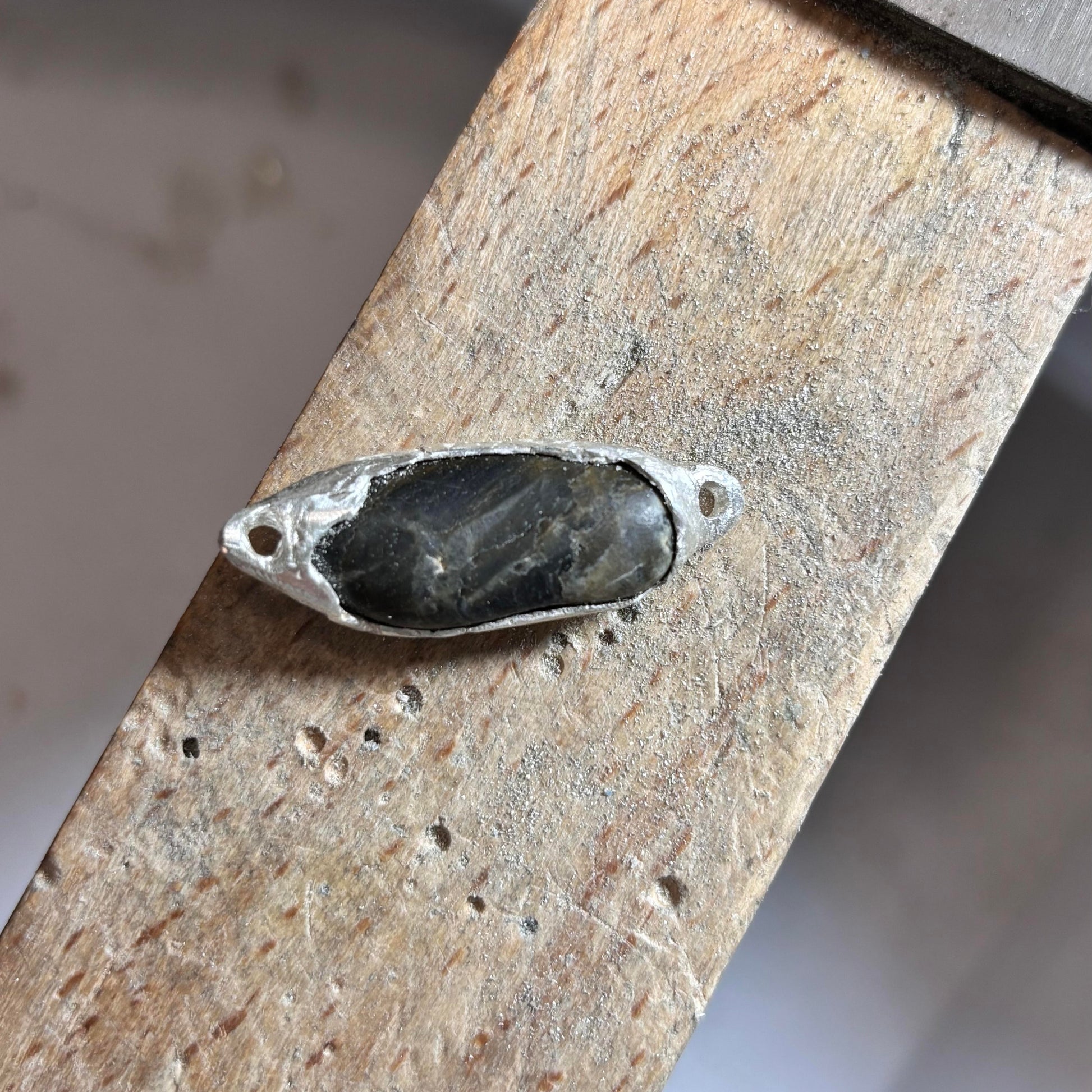 Silver ring with a dark stone on a wooden surface