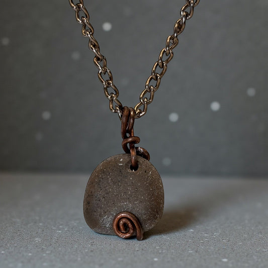 Necklace with a pendant featuring a stone and copper spiral on a gray background