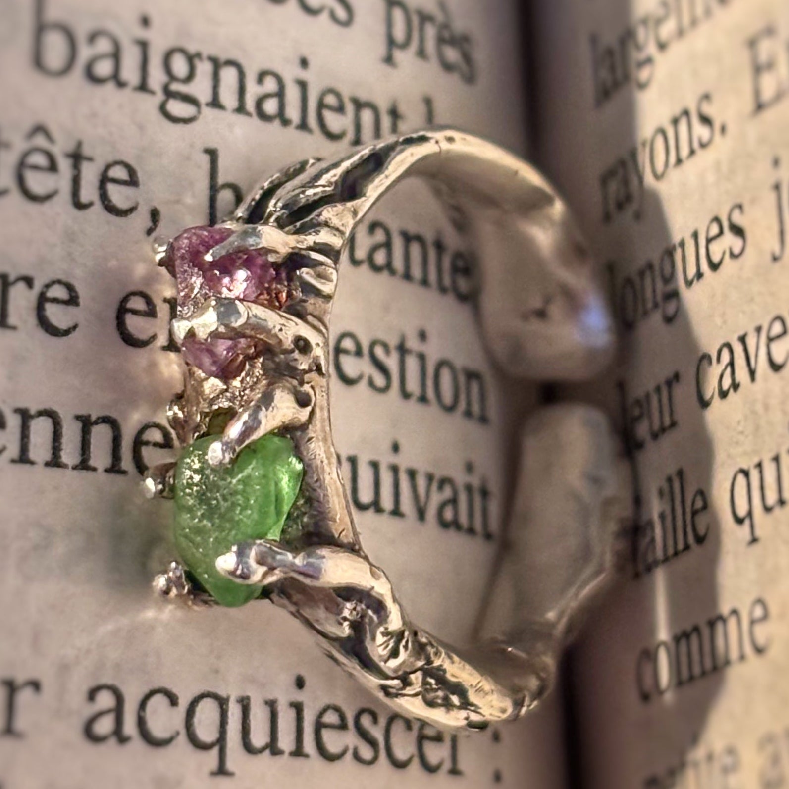 Silver ring with green and pink gemstones on an open book