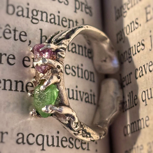 Silver ring with green and pink gemstones on an open book