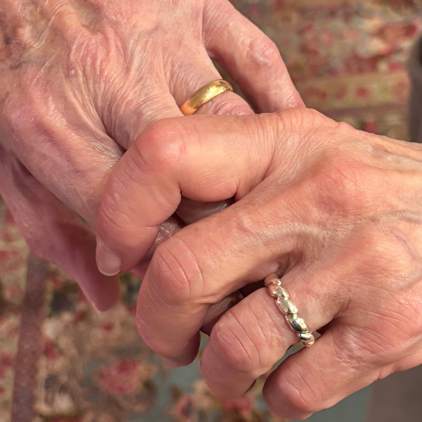 Close-up of two hands holding each other, wearing rings (gold and silver)