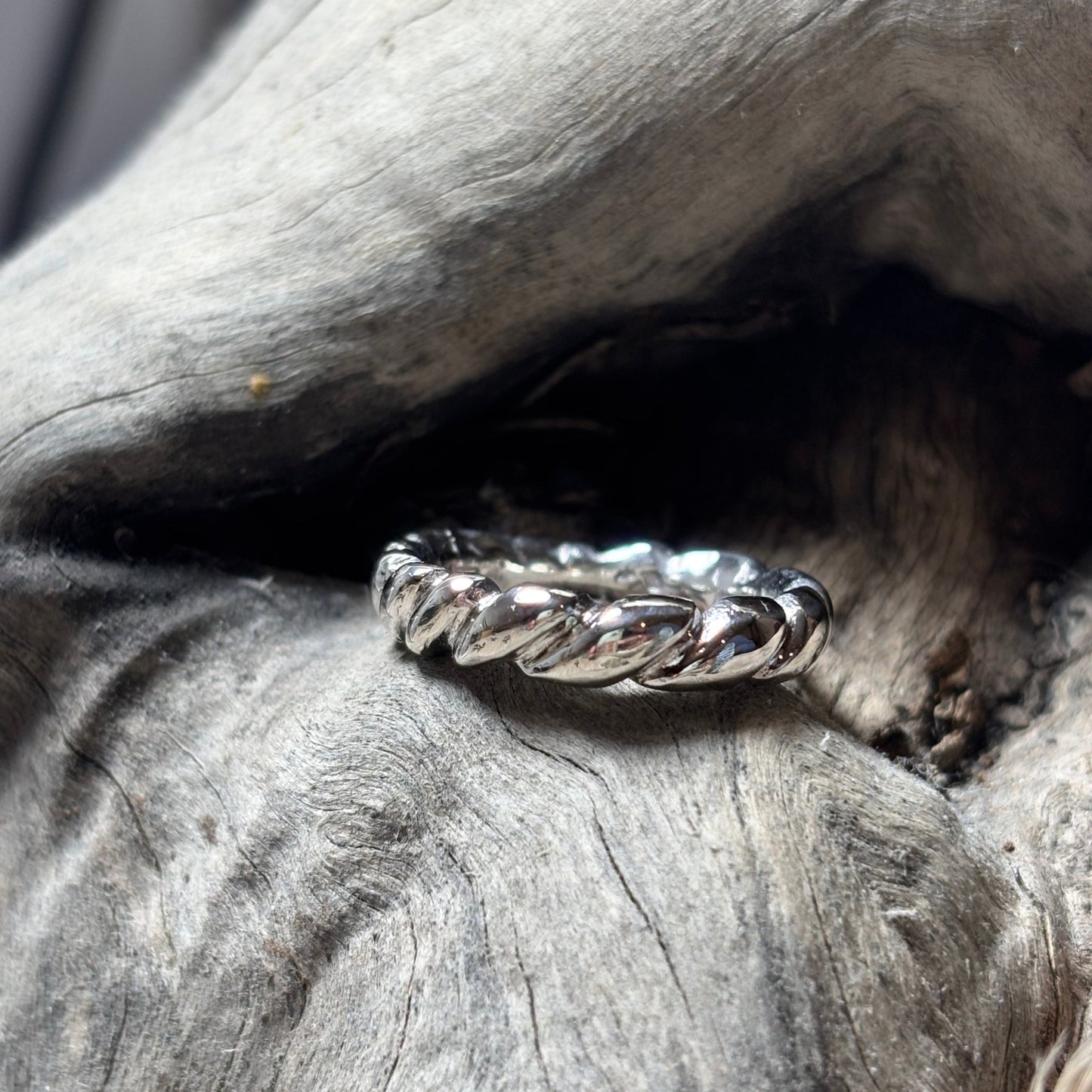 Silver ring with braided design on a textured wooden surface