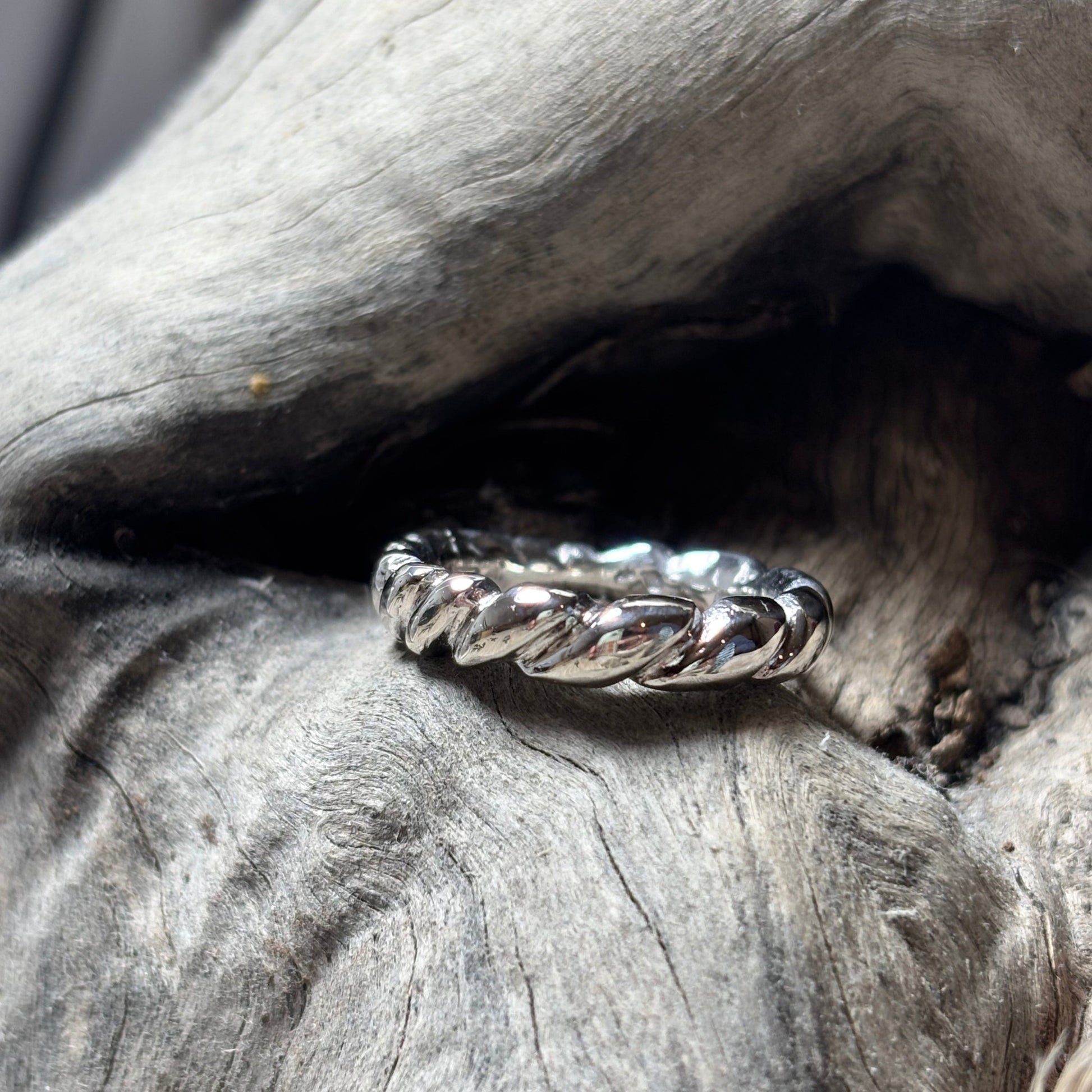 Silver ring with braided design on a textured wooden surface