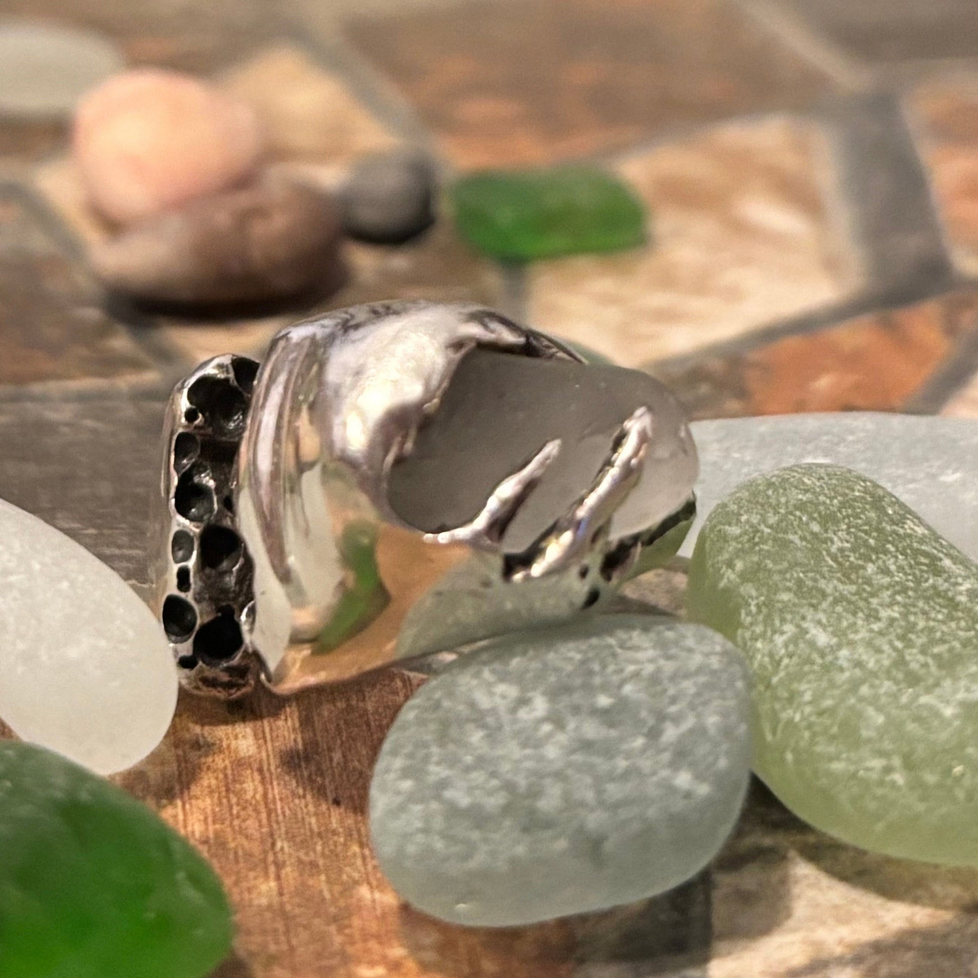 Close-up of a silver ring with green and brown stones on a textured surface.