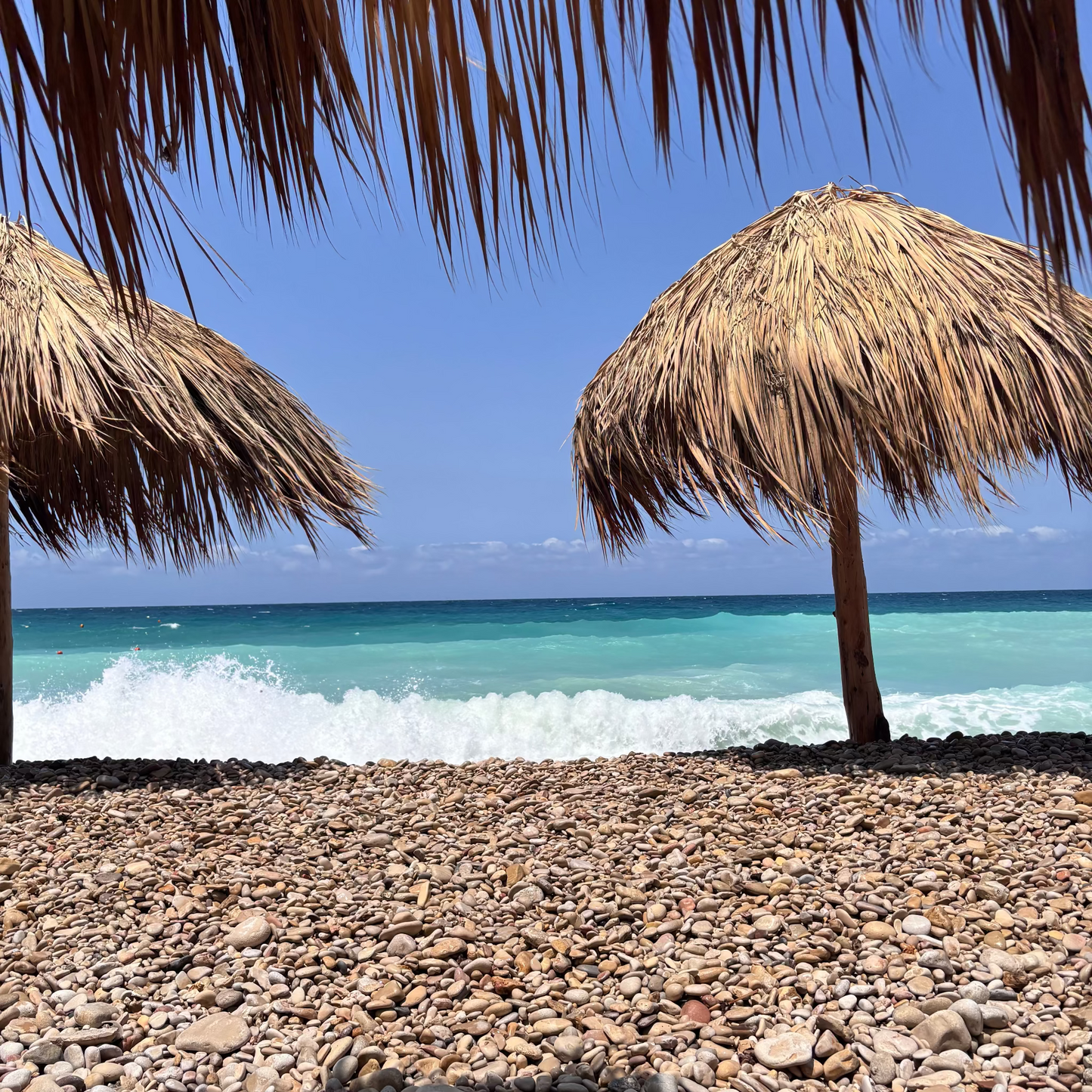 Beach scene with thatched umbrellas and turquoise ocean under a clear blue sky.