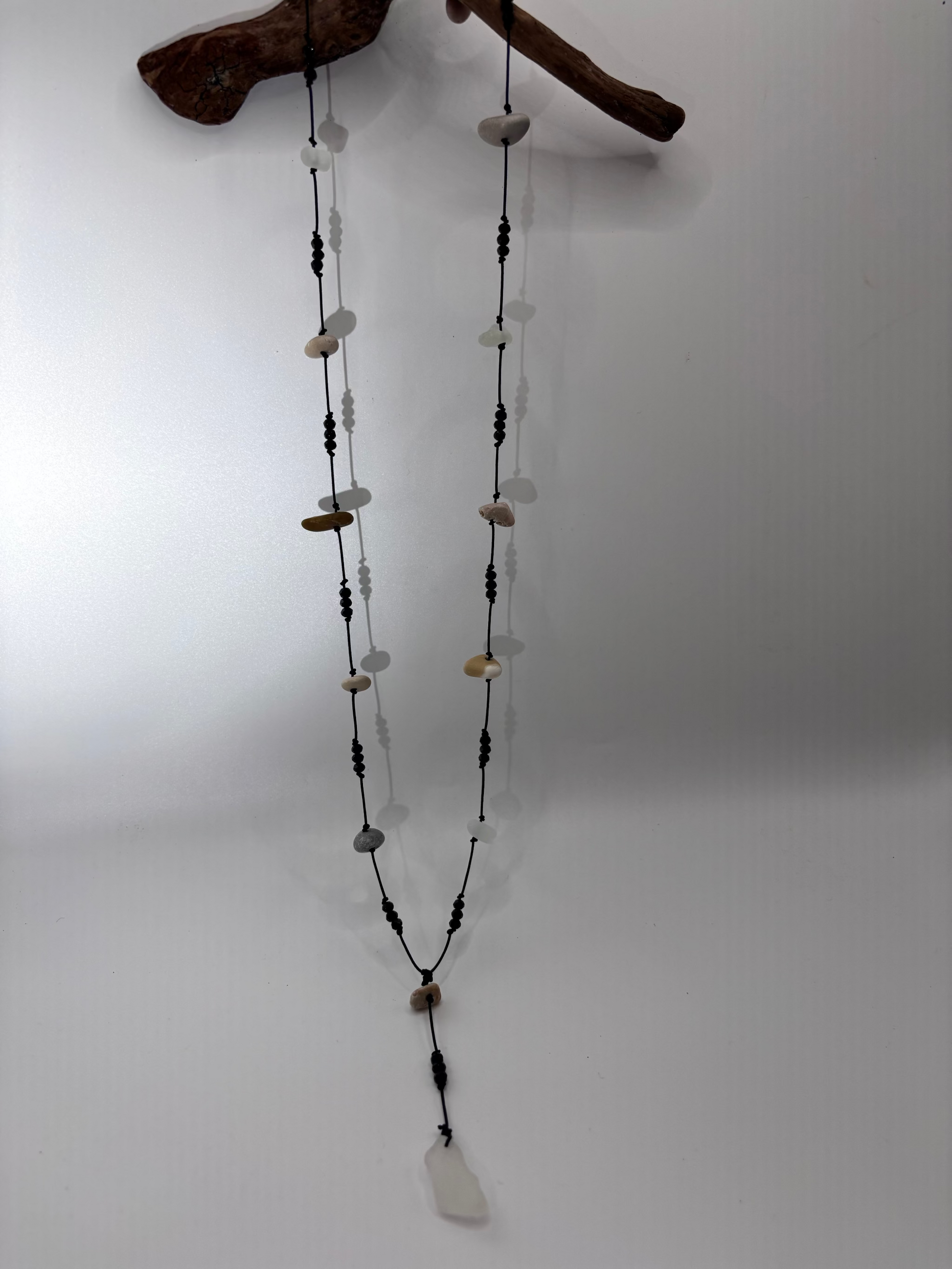 Long necklace with various beads hanging from a branch on a white background