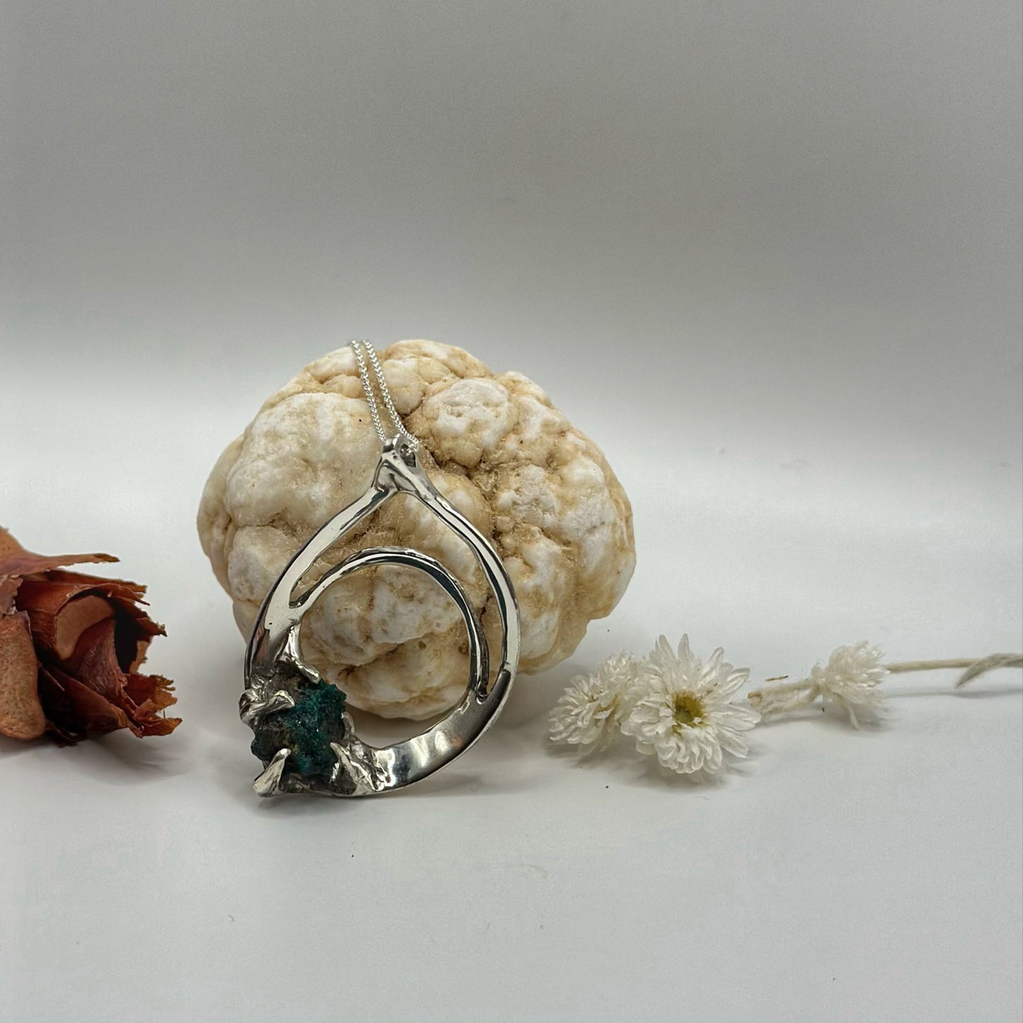 Silver necklace with a pendant on a textured surface with flowers with raw dioptase