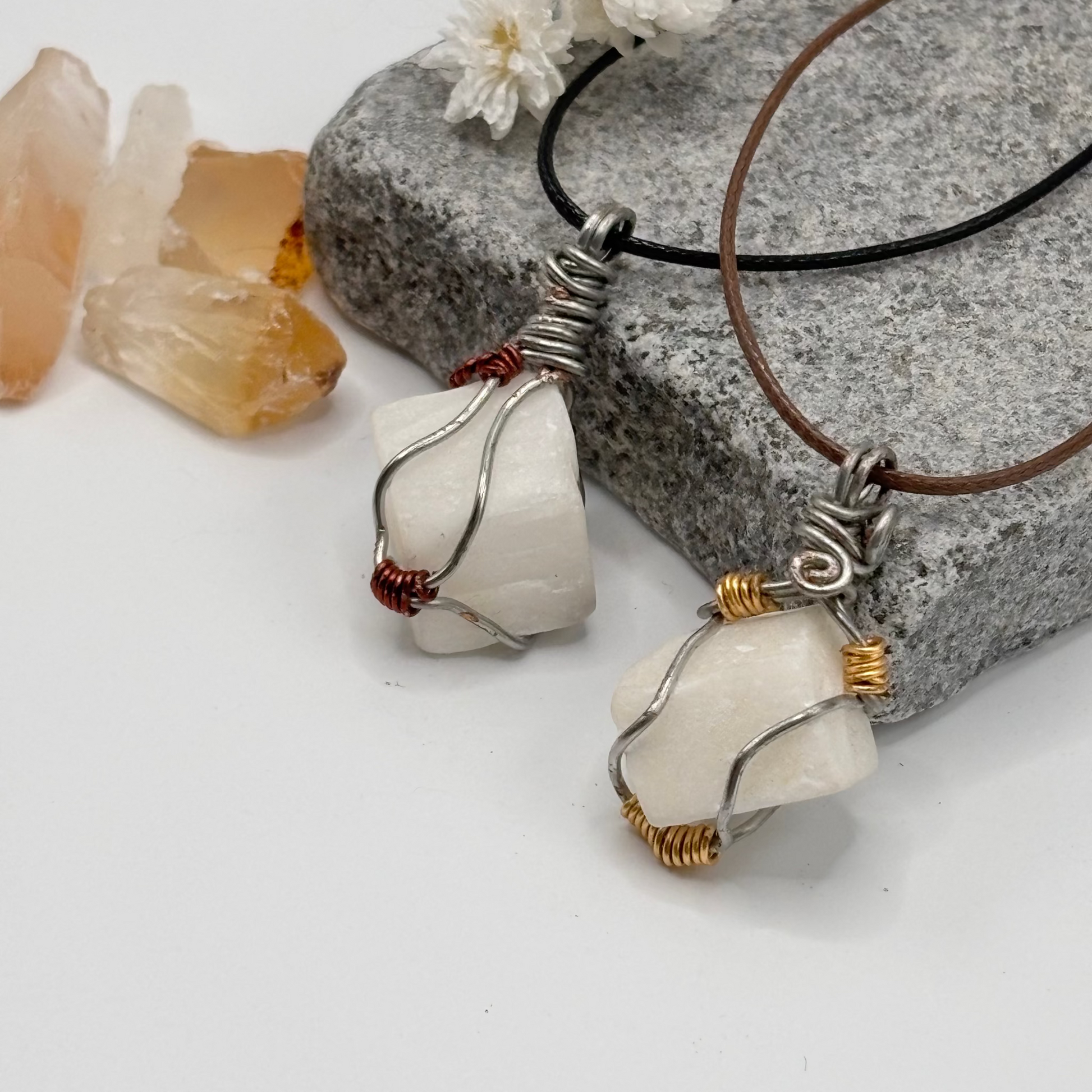 Two white square stone pendants on necklaces with crystals and flowers in the background
