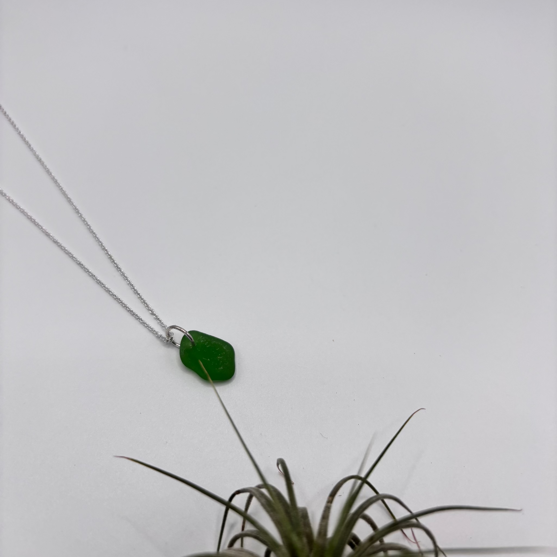Green sea glass pendant with raw, tide-shaped edges, set in silver and hanging on a delicate silver chain, capturing the natural movement and glow of the sea.
