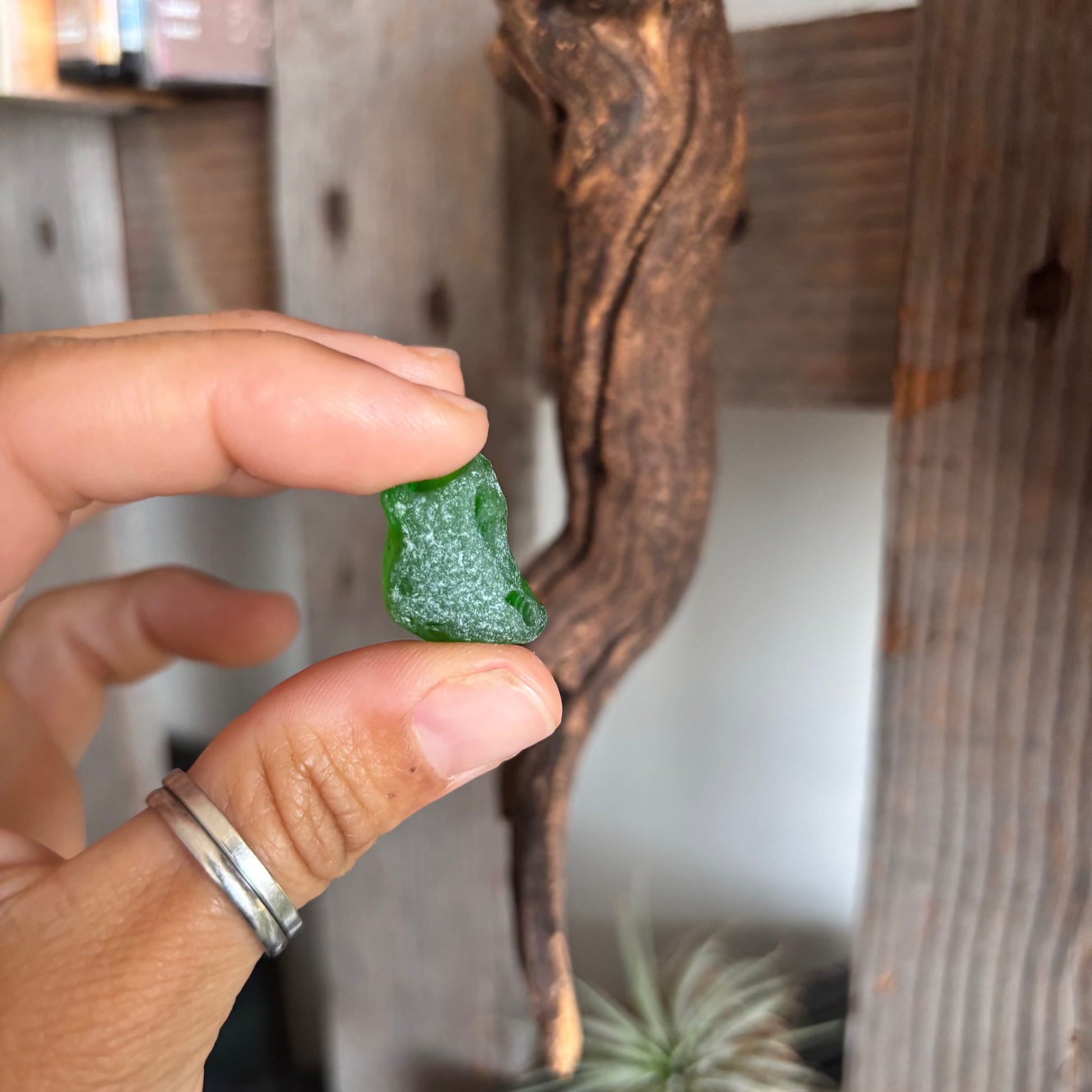 Hand holding a green sea glass against a wooden background
