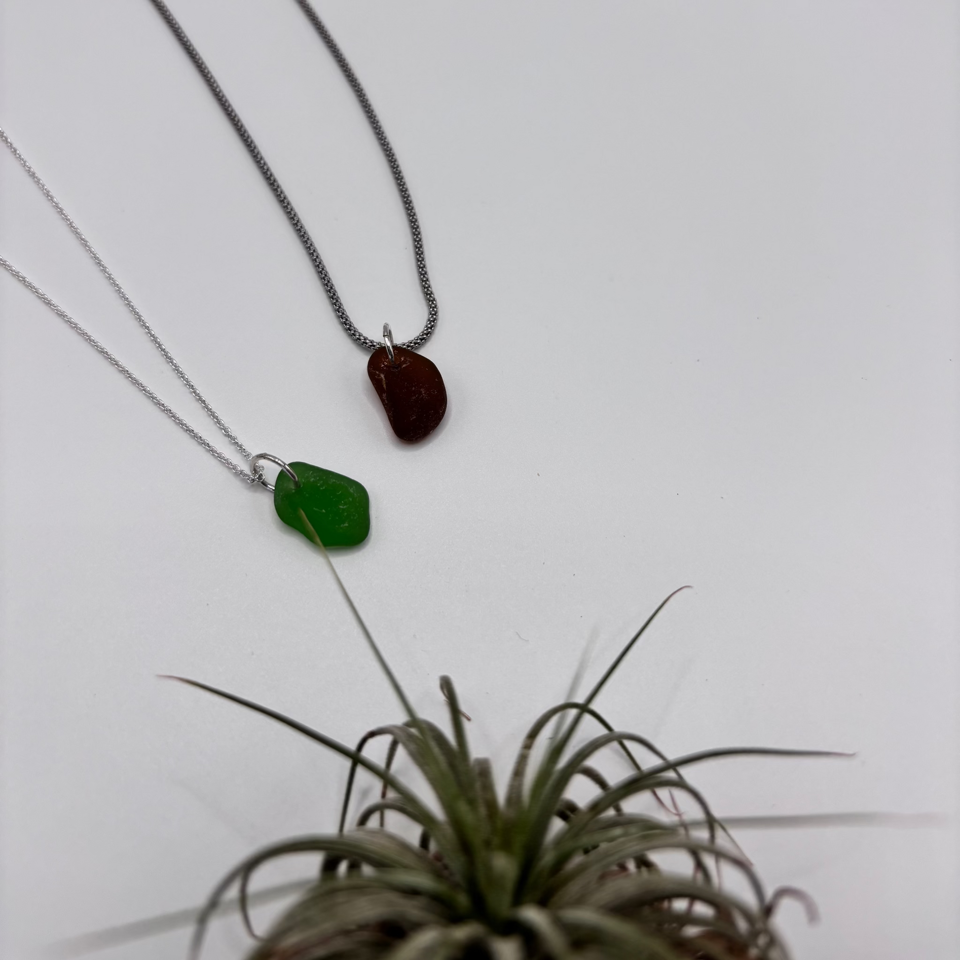Green and brown sea glass pendant with raw, tide-shaped edges, set in silver and hanging on a delicate rhodium-plated chain, capturing the natural movement and story from the sea.
