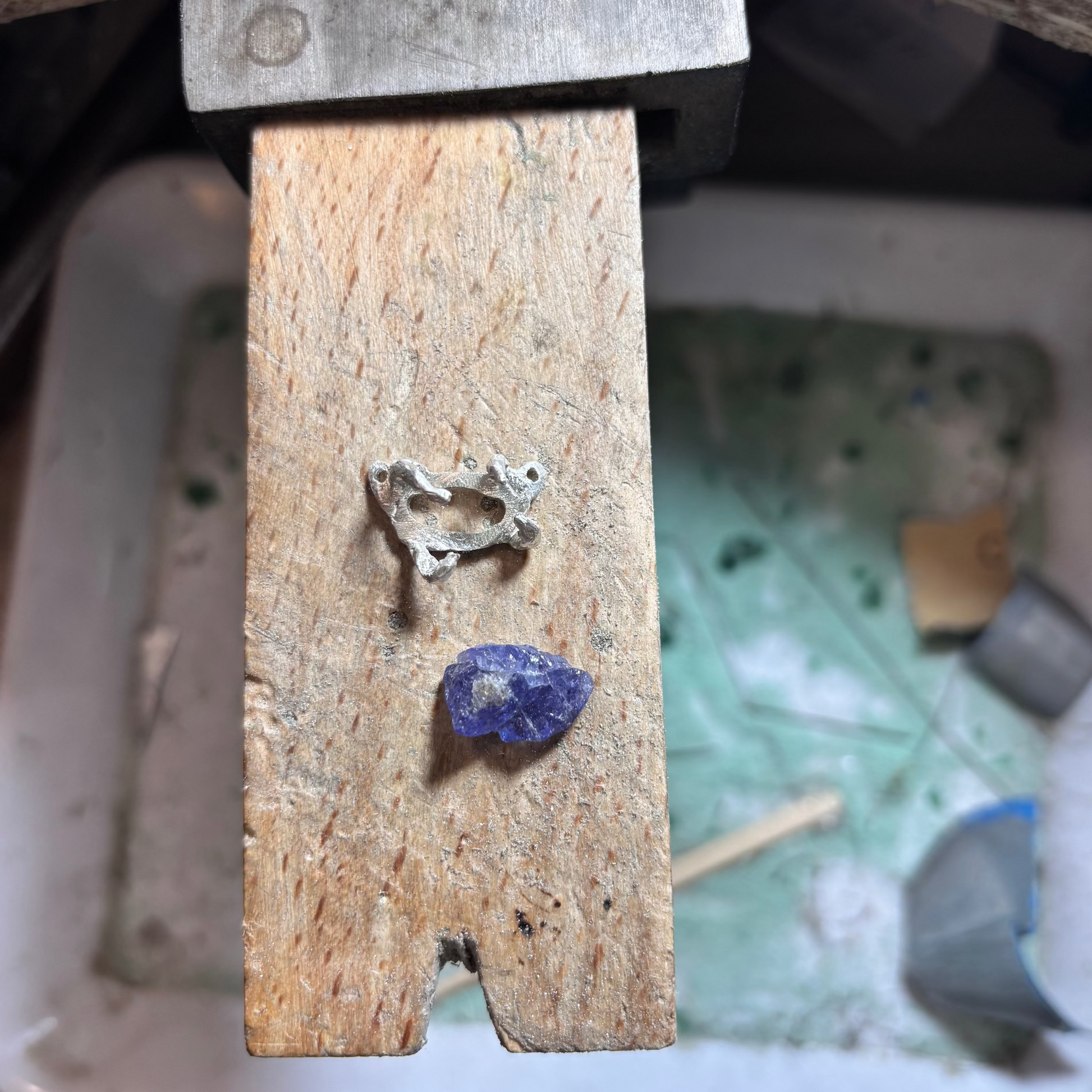 Raw tanzanite stone held in silver claws, crafted with the lost wax technique, showing deep violet and blue tones, suspended on a silver chain with four silver claws.