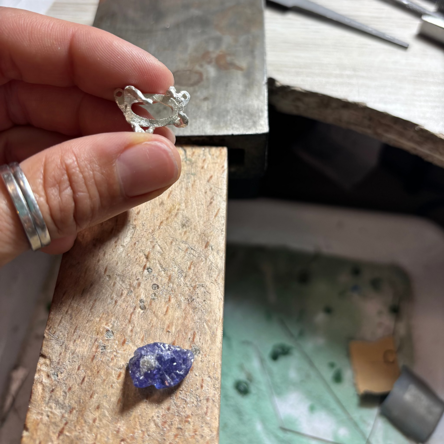 Raw tanzanite stone to be held in silver claws, crafted with the lost wax technique, showing deep violet and blue tones, suspended on a silver chain with four silver claws.