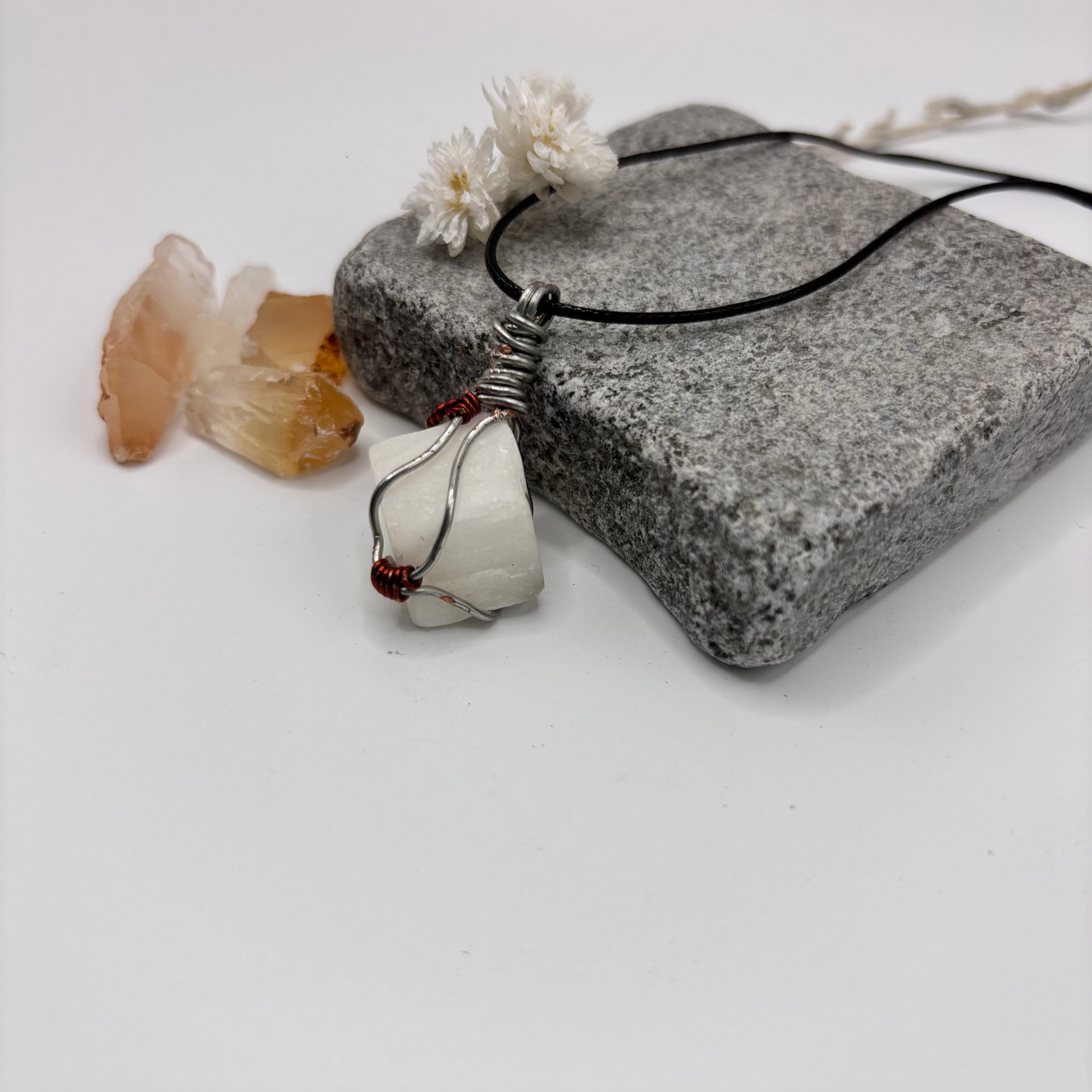 Necklace with a pendant on a stone surface with crystals and flowers.