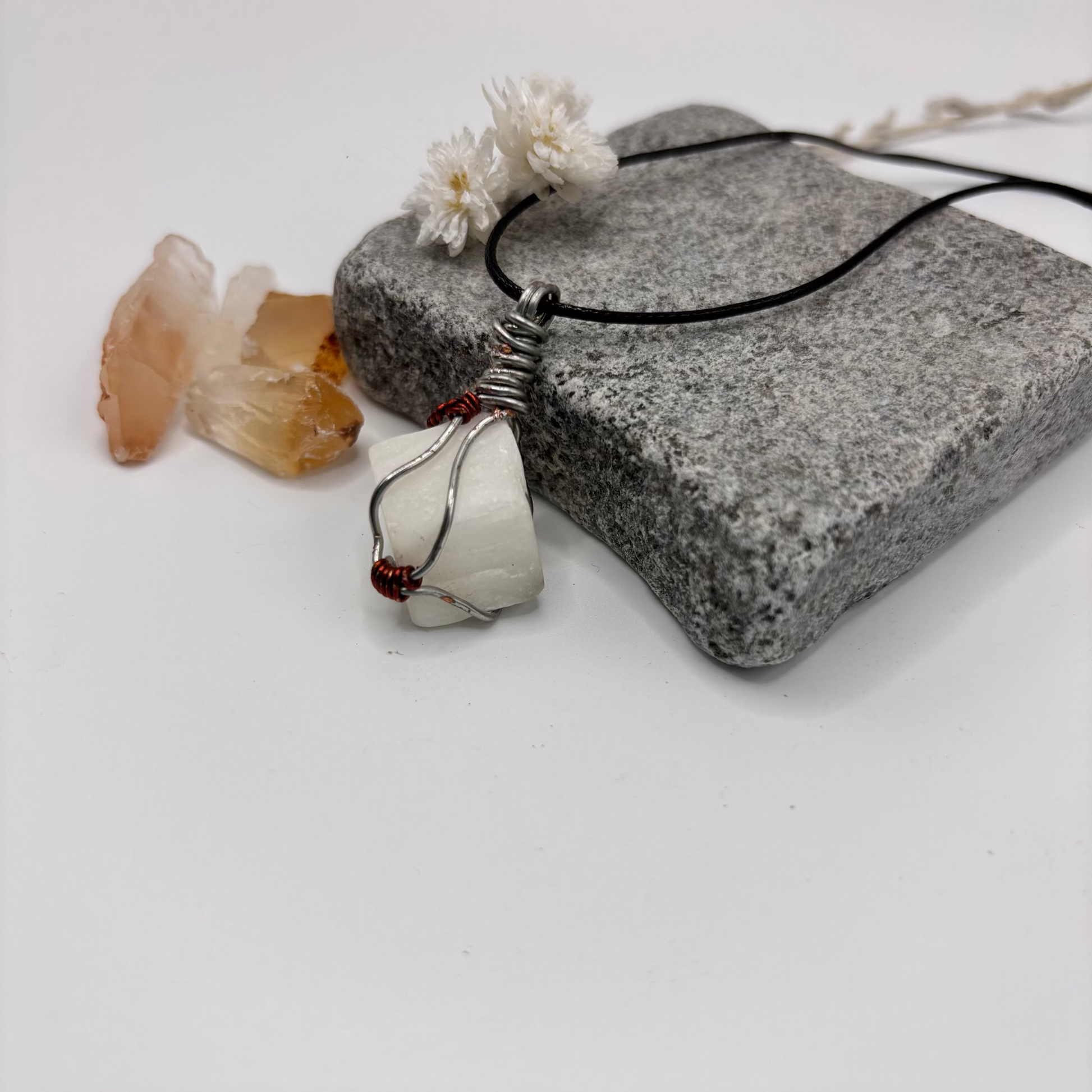 Necklace with a pendant on a stone surface with crystals and flowers.