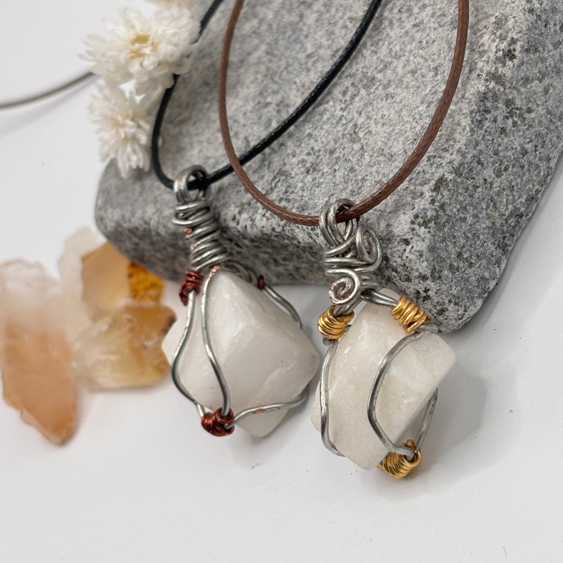Two necklaces with white stone pendants on a stone surface.