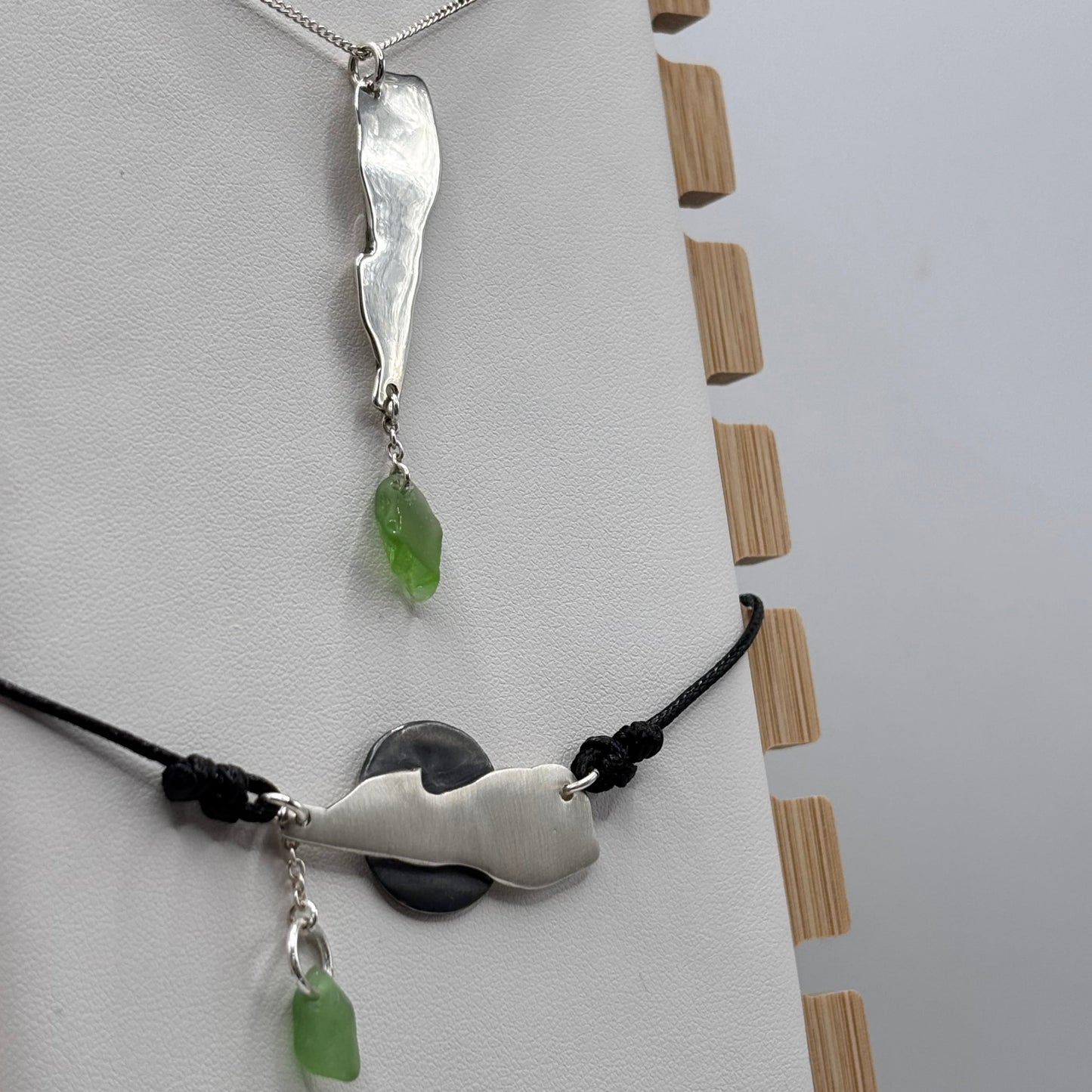 Two silver pendants with green beads on a white surface