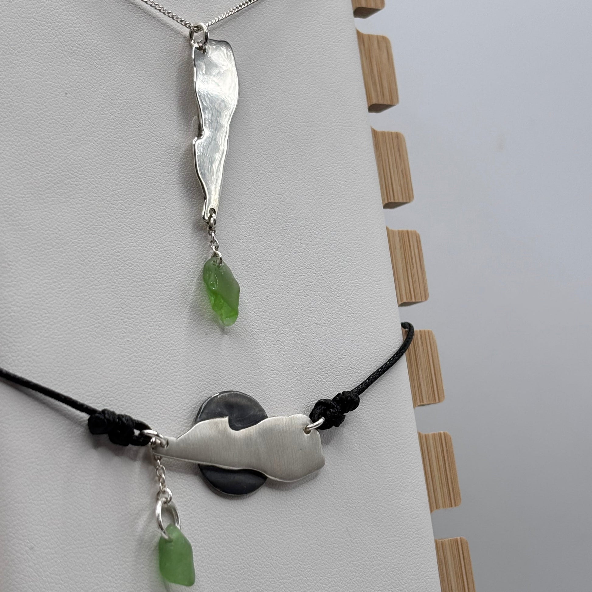 Two silver pendants with green beads on a white surface