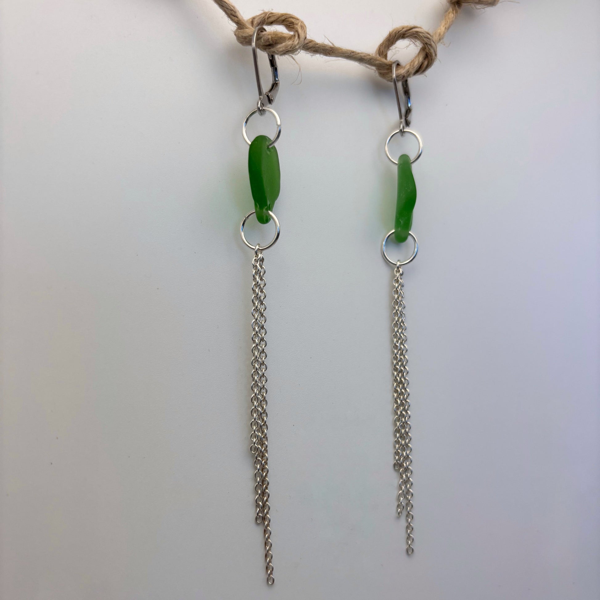 Handcrafted earrings featuring green sea glass and flowing silver wire drops.