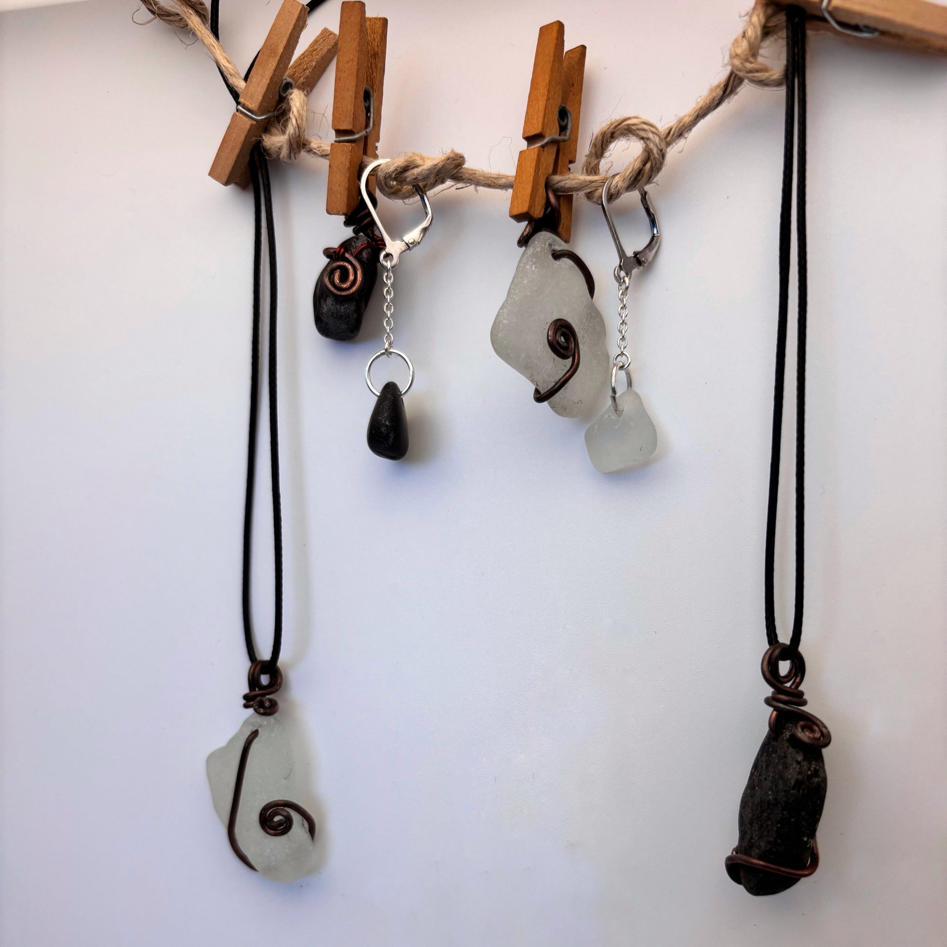 Pair of handcrafted silver earrings, 2.5 cm long. One features white sea glass, the other a small black beach stone. pendants tat can go along with the vibes.