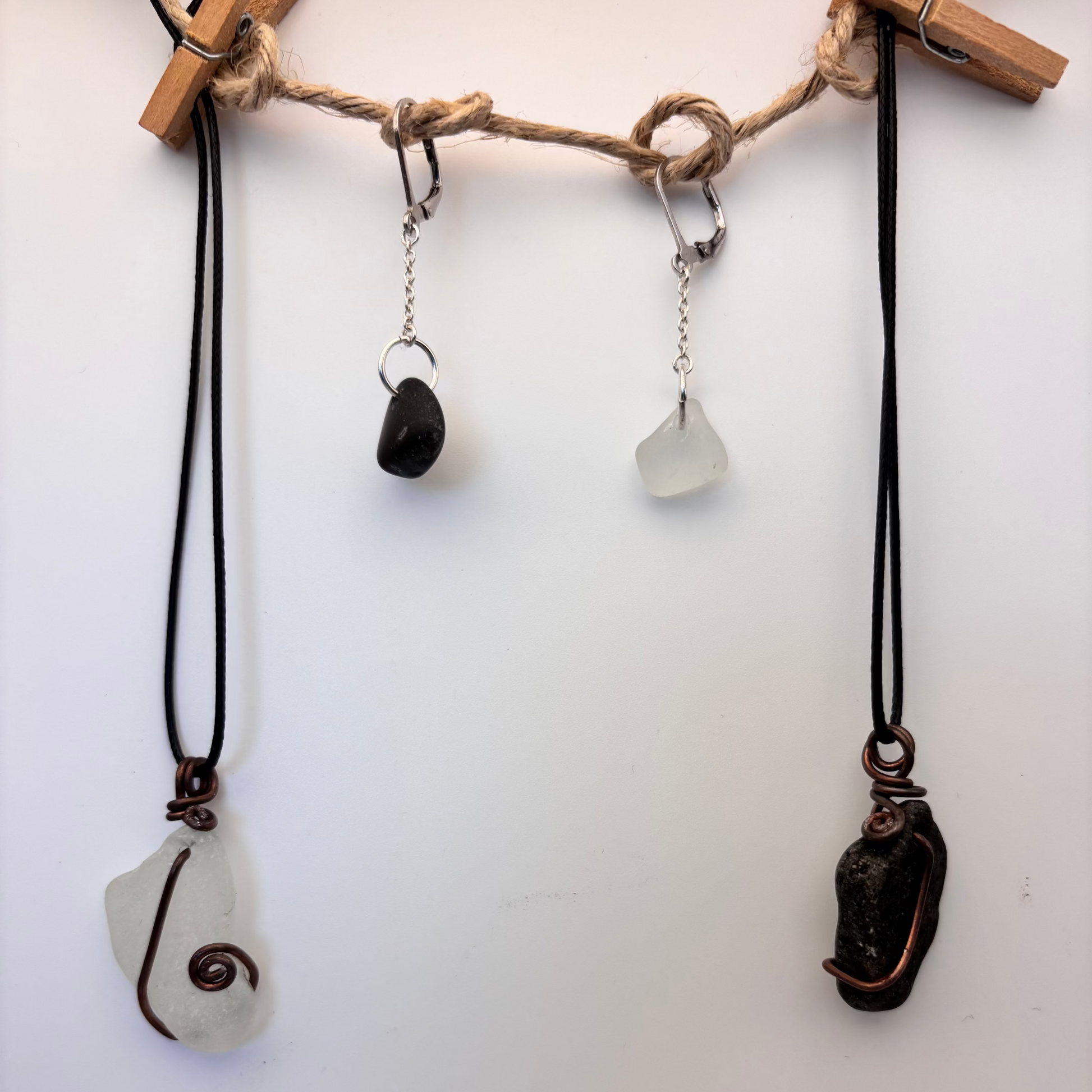 Pair of handcrafted silver earrings, 2.5 cm long. One features white sea glass, the other a small black beach stone.