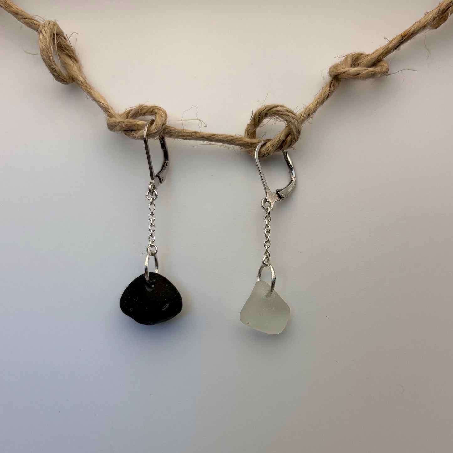 Pair of handcrafted silver earrings, 2.5 cm long. One features white sea glass, the other a small black beach stone.