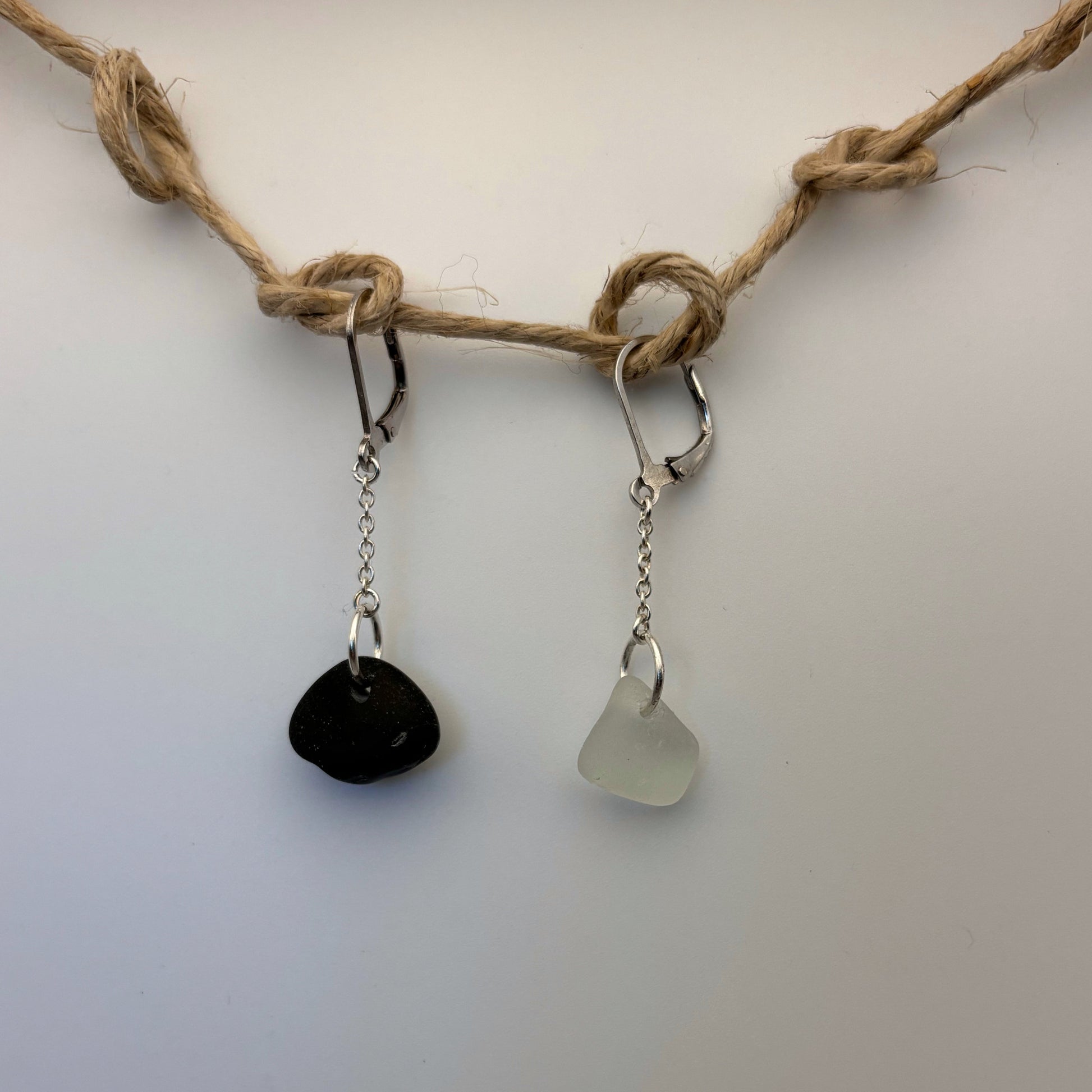 Pair of handcrafted silver earrings, 2.5 cm long. One features white sea glass, the other a small black beach stone.