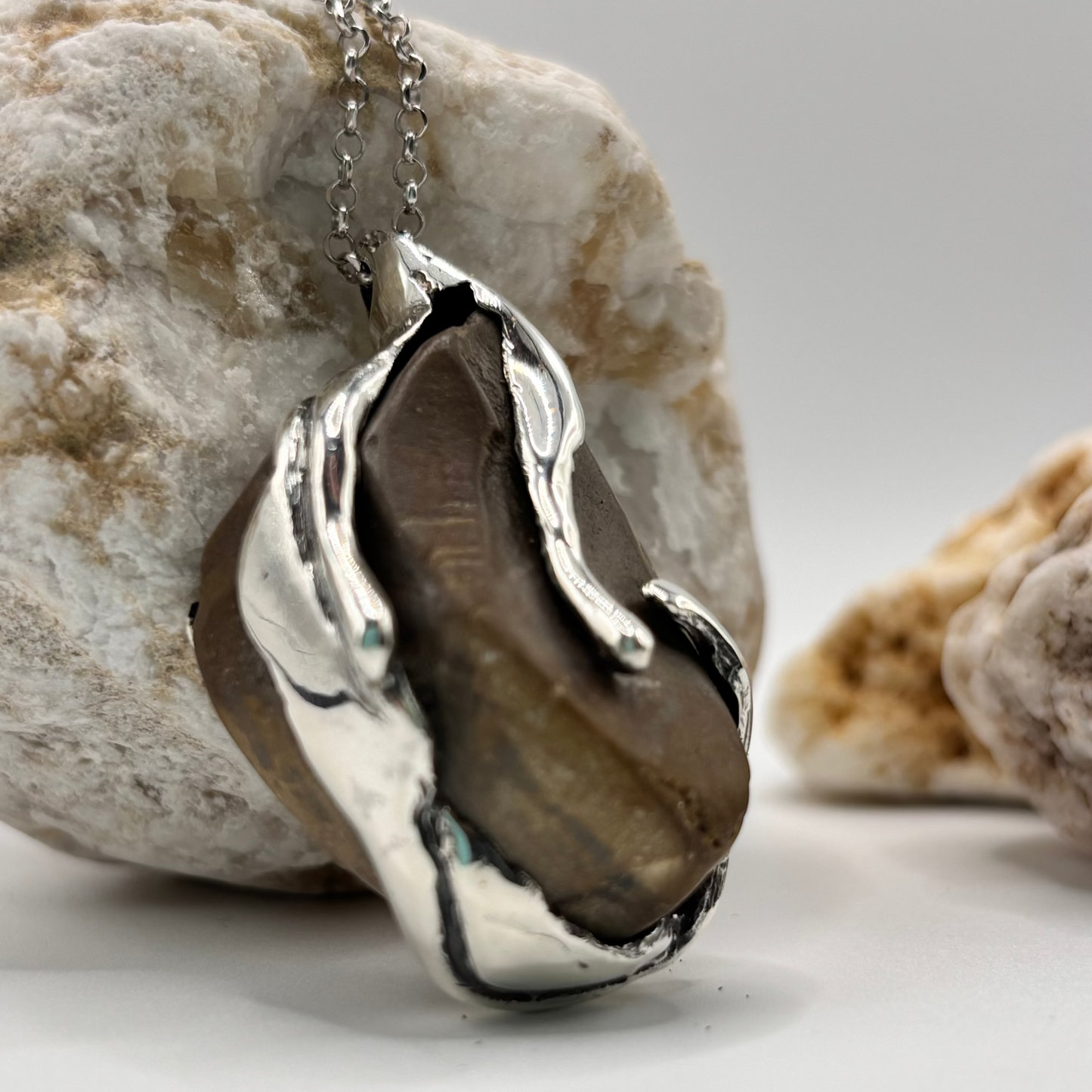 Close-up of a handmade pendant with a raw beach stone encased in an organic silver design.