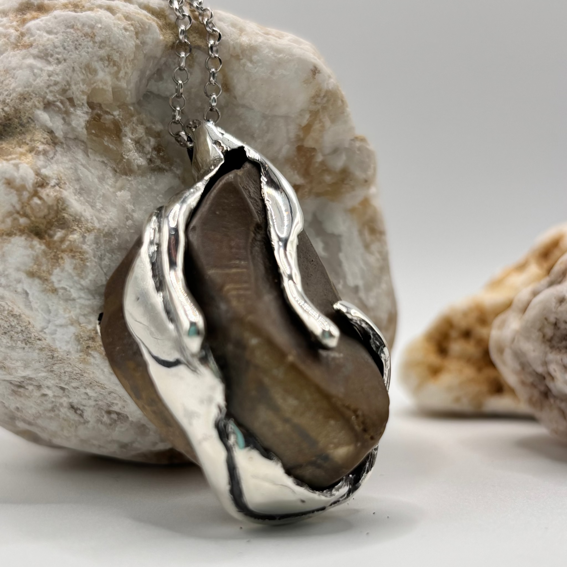 Close-up of a handmade pendant with a raw beach stone encased in an organic silver design.