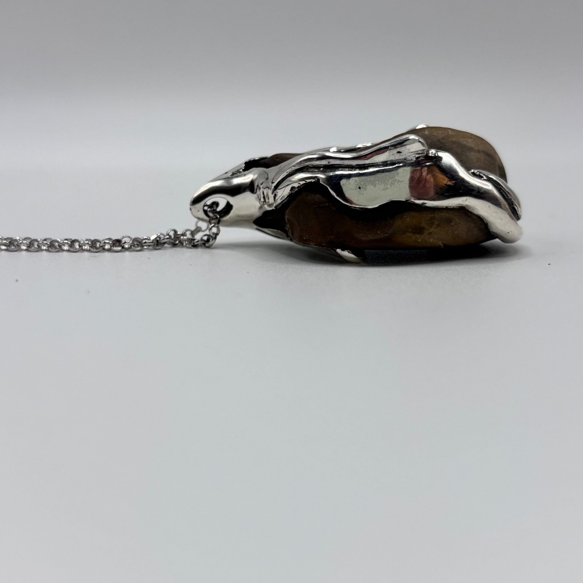 Close-up of a handmade pendant with a raw beach stone encased in an organic silver design.