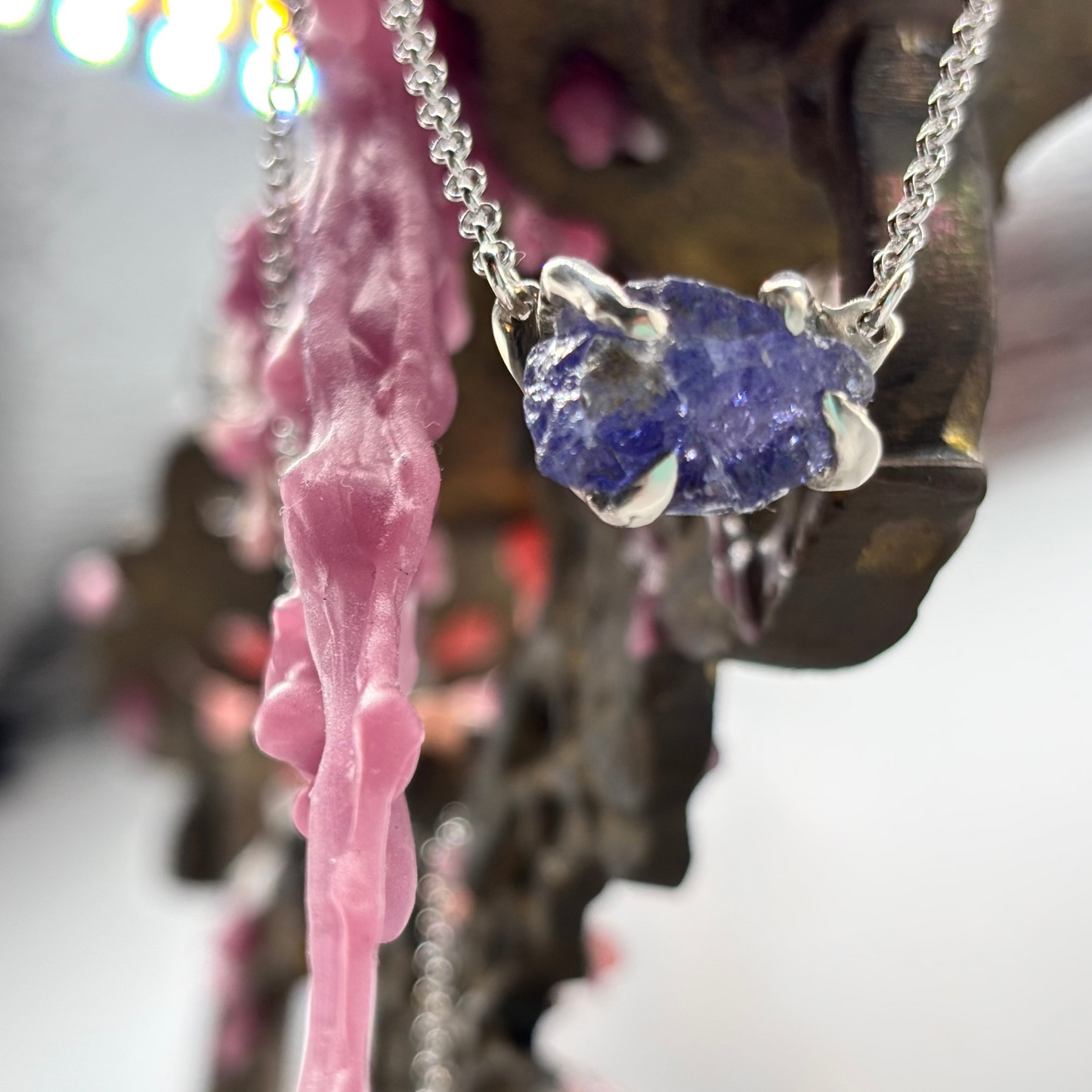 Raw tanzanite stone held in silver claws, crafted with the lost wax technique, showing deep violet and blue tones, suspended on a silver chain.