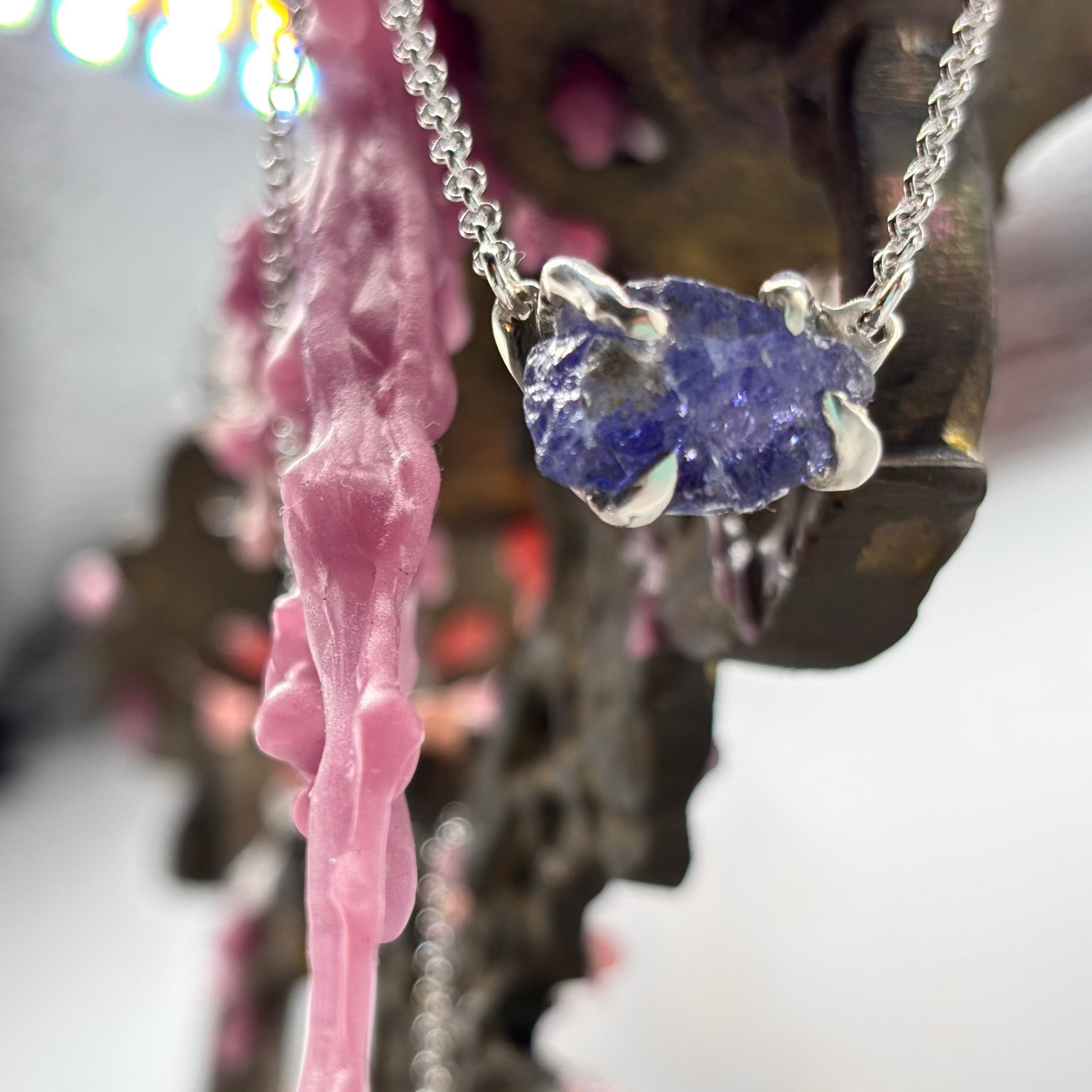 Raw tanzanite stone held in silver claws, crafted with the lost wax technique, showing deep violet and blue tones, suspended on a silver chain.