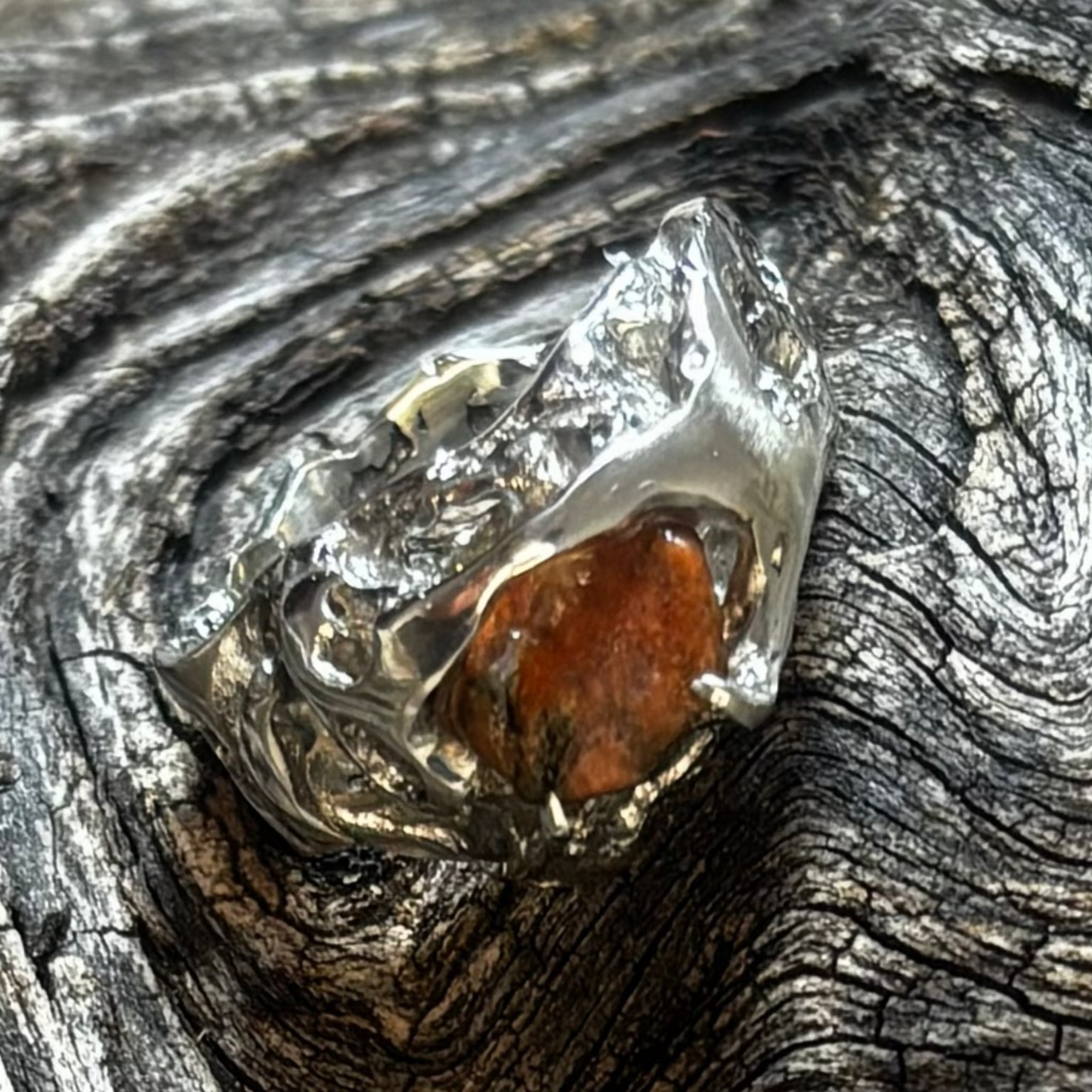 Silver ring with a brown stone on a textured wooden surface
