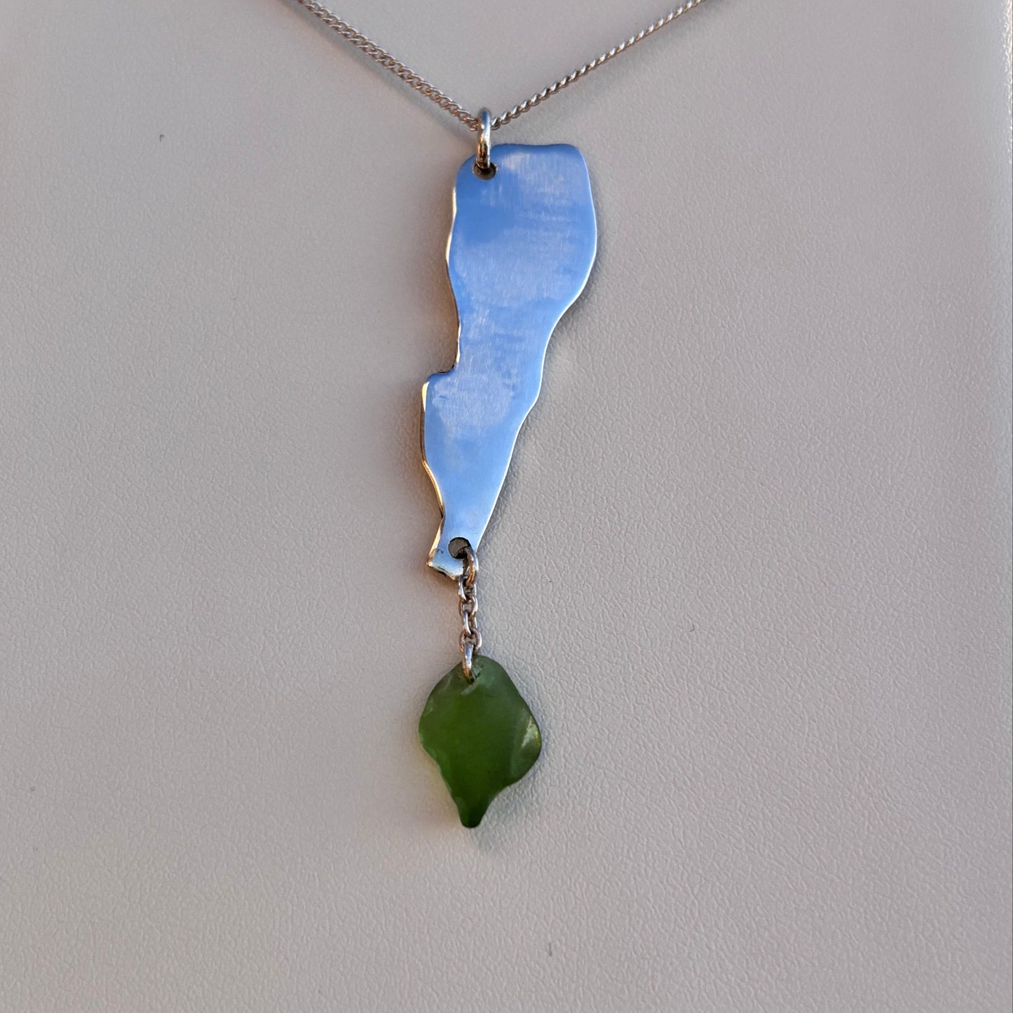 Necklace with a silver pendant and green sea glass on a light gray background