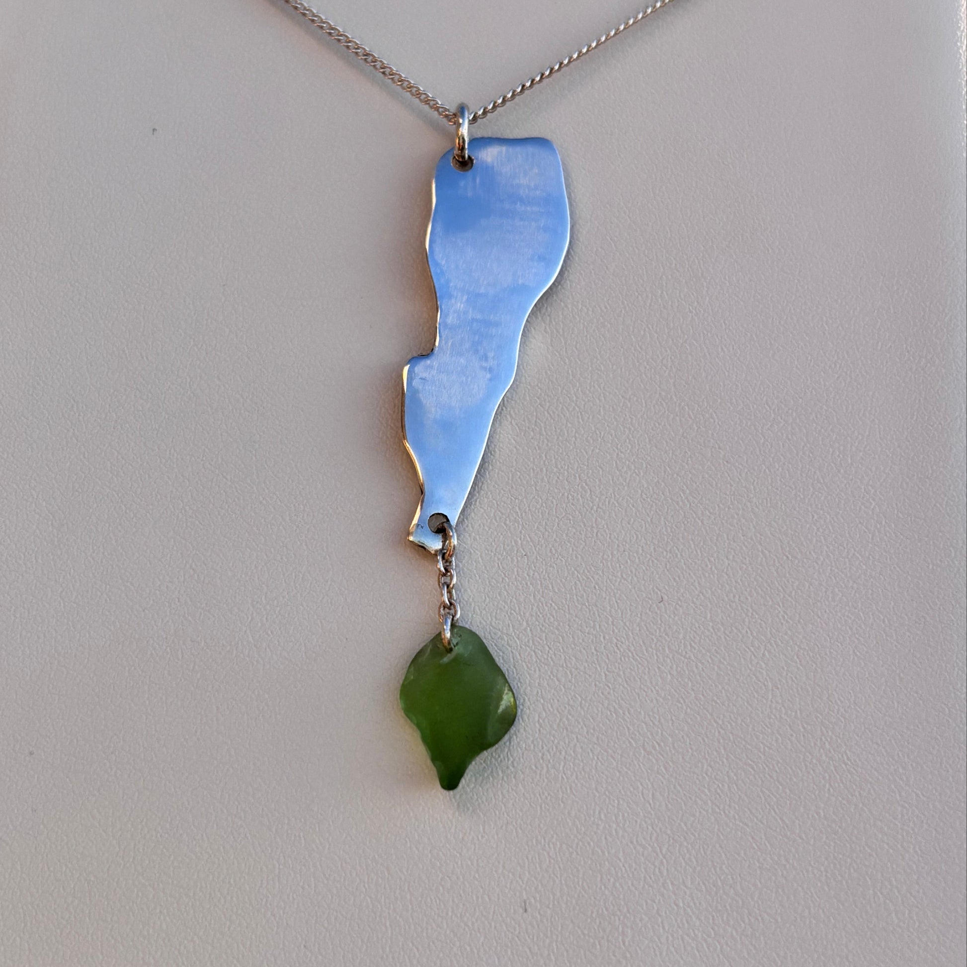 Necklace with a silver pendant and green sea glass on a light gray background