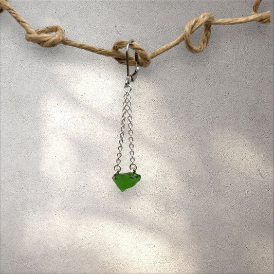 Green heart-shaped pendant on a chain, hanging from a piece of twine against a light background