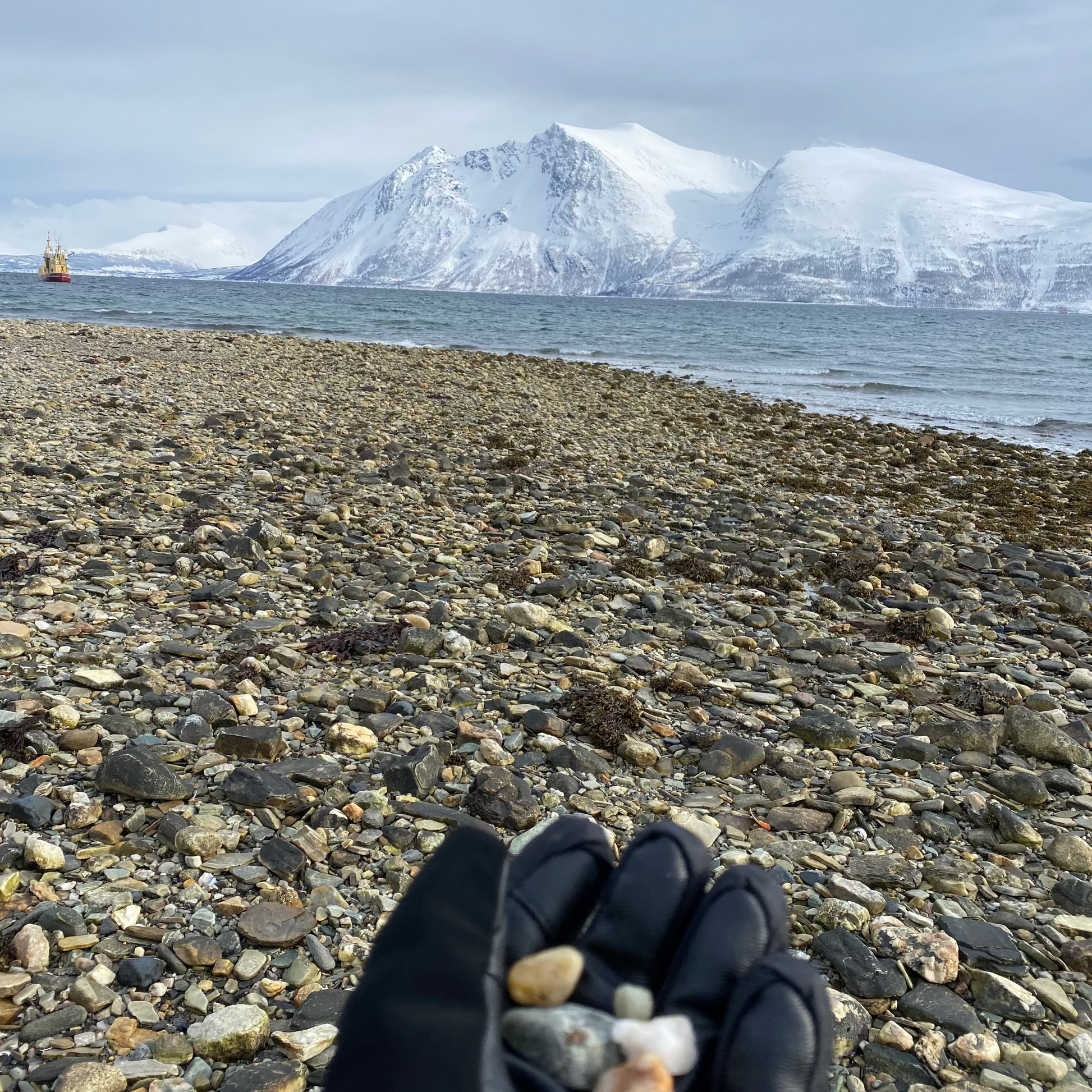 Hand holding small stones with a scenic view of mountains and water in the background