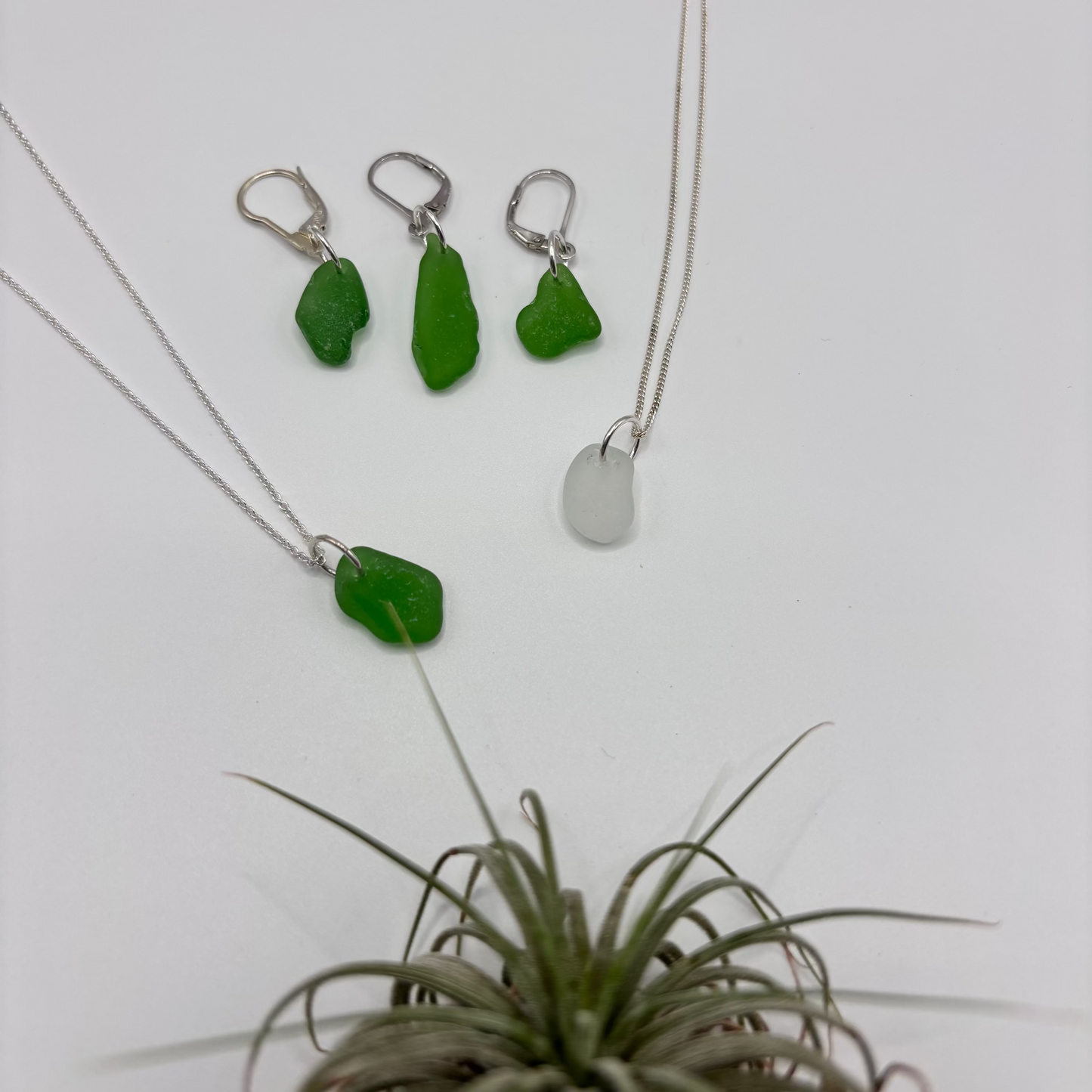 Green and white sea glass pendant with raw, tide-shaped edges, set in silver and hanging on a silver chain, capturing the natural movement and translucent glow of the sea. also three earrings silver with green sea glass.
