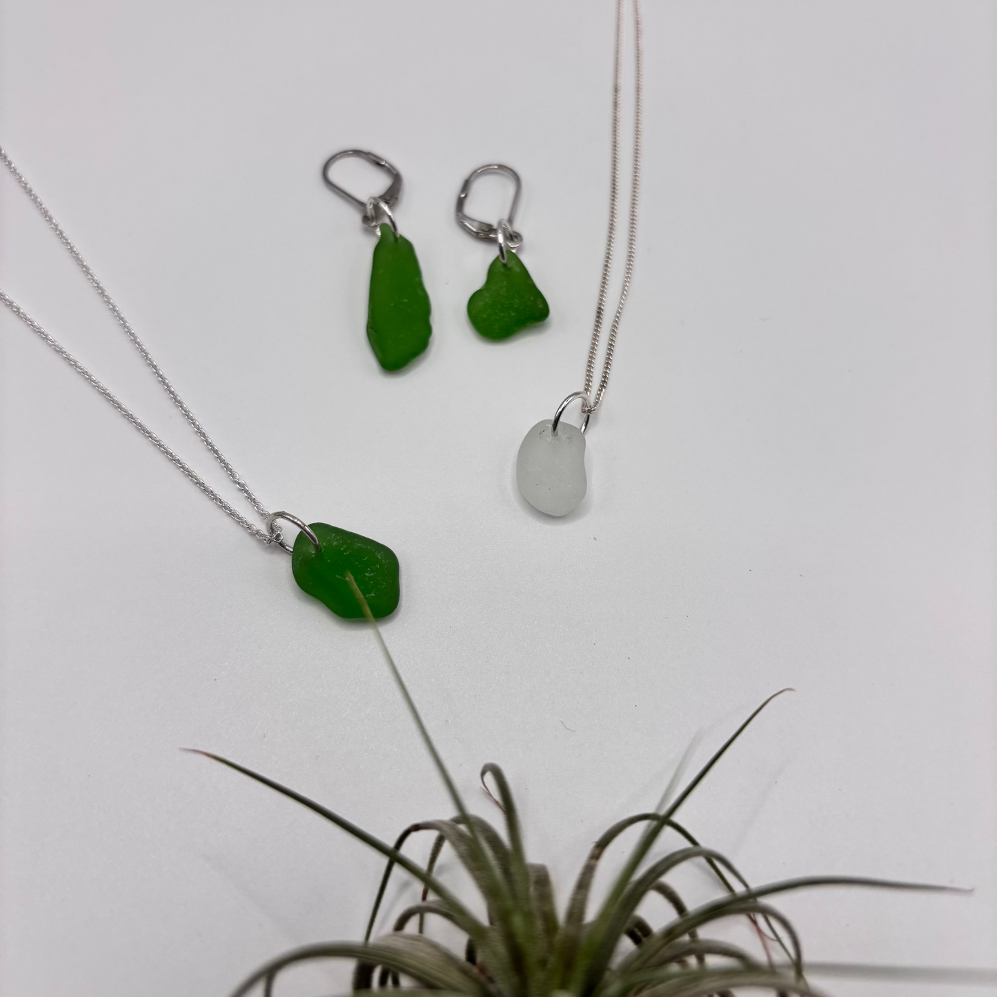 Green and white sea glass pendant with raw, tide-shaped edges, set in silver and hanging on a silver chain, capturing the natural movement and translucent glow of the sea.
