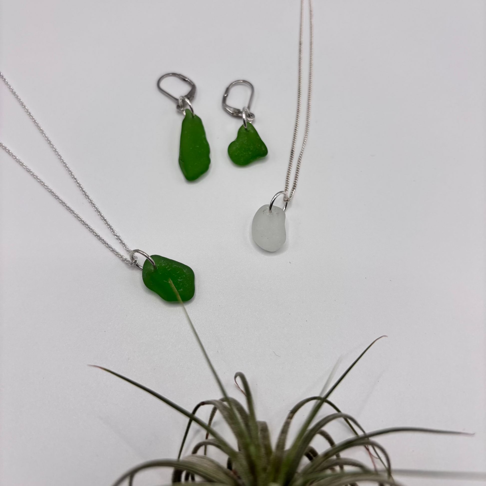 Green and white sea glass pendant with raw, tide-shaped edges, set in silver and hanging on a silver chain, capturing the natural movement and translucent glow of the sea.
