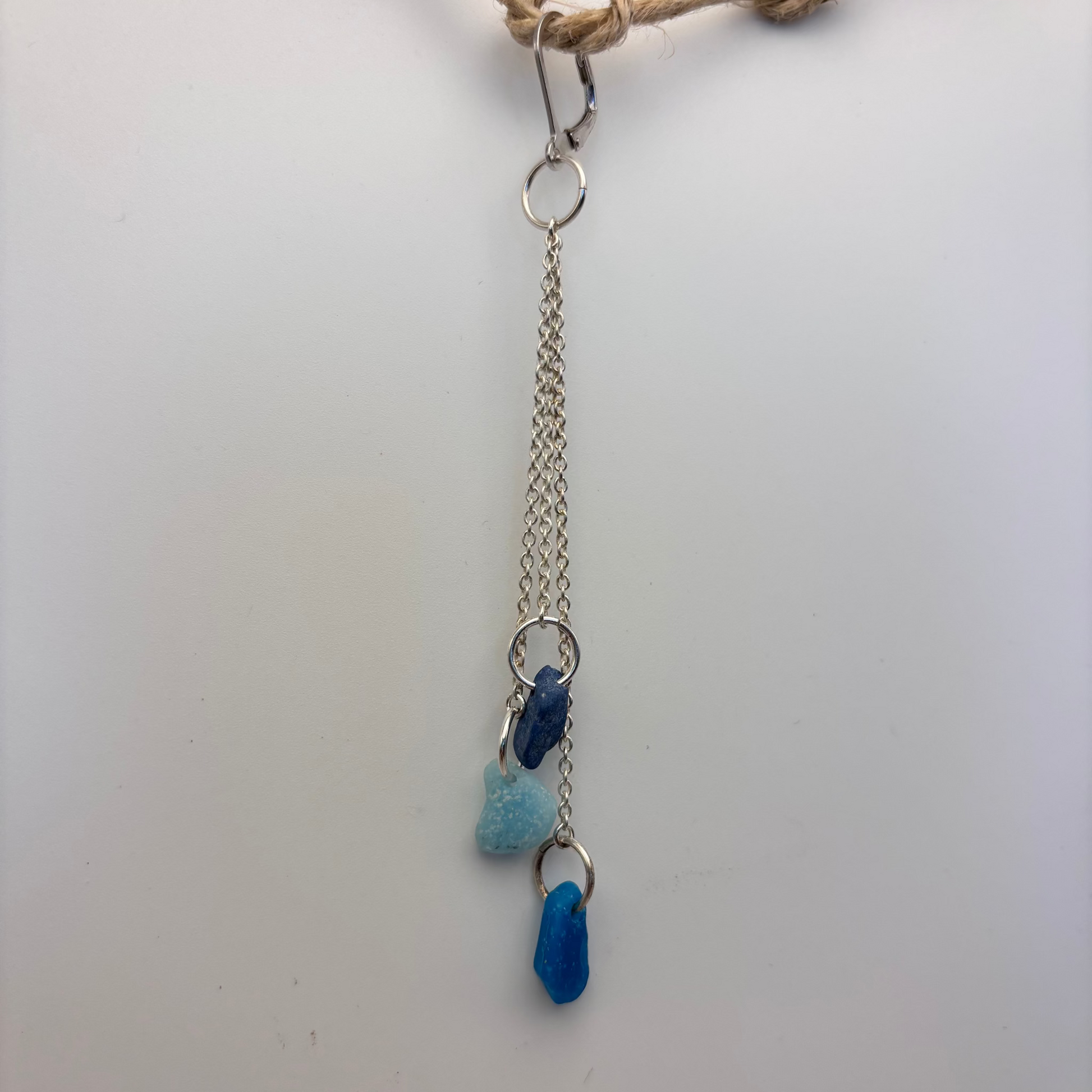 Single earring with three beach-found blue fragments hanging on thin silver threads, soft natural light highlighting the different shades of blue.